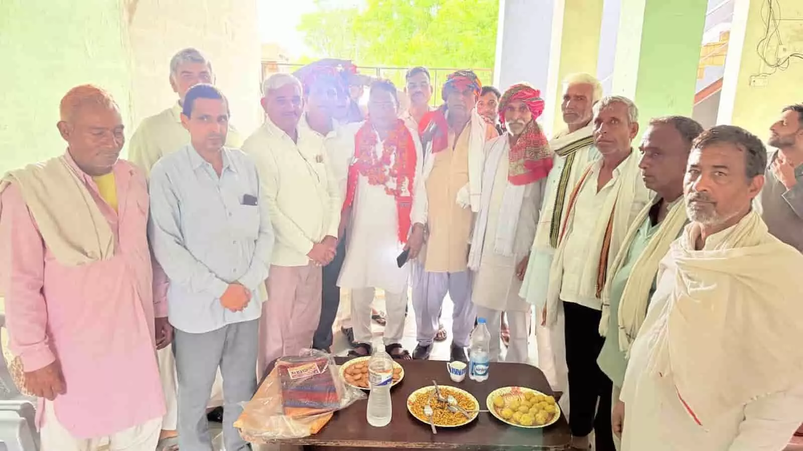 तस्वीर में फूलमाला पहने व्यक्ति के साथ कई लोग भवन के अंदर खड़े हैं। तस्वीर में फूलमाला पहने व्यक्ति के साथ कई लोग भवन के अंदर खड़े हैं।