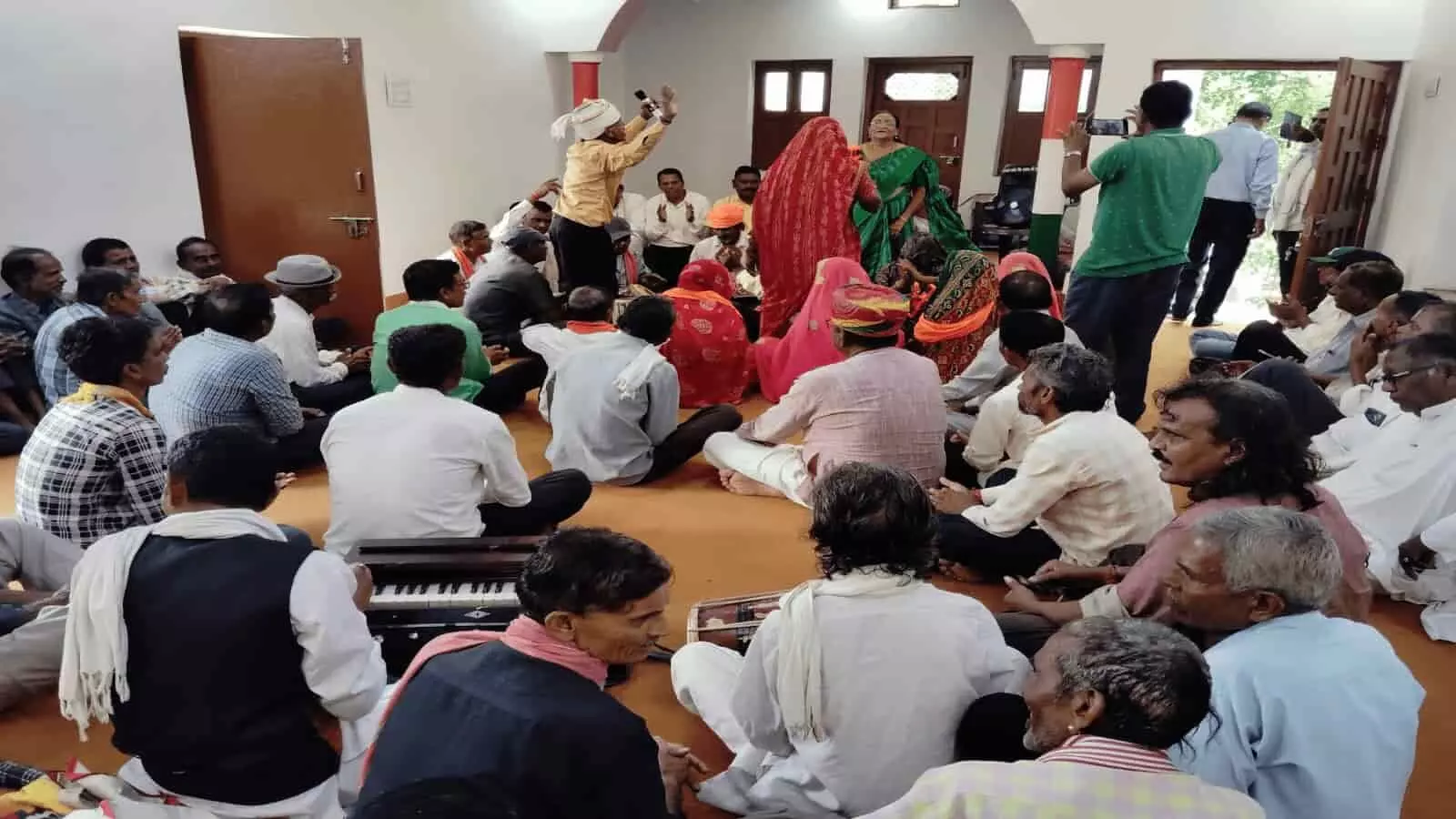 तस्वीर में खेरवाड़ा कार्यालय में आदिवासी दिवस कार्यक्रम के दौरान बैठे लोग और कलाकार नजर आ रहे हैं। तस्वीर में खेरवाड़ा कार्यालय में आदिवासी दिवस कार्यक्रम के दौरान बैठे लोग और कलाकार नजर आ रहे हैं।