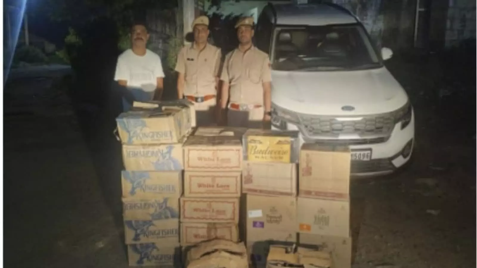 तस्वीर में पुलिसकर्मी और व्यक्ति सफेद कार के पास जब्त शराब के कार्टन के साथ खड़े हैं। तस्वीर में पुलिसकर्मी और व्यक्ति सफेद कार के पास जब्त शराब के कार्टन के साथ खड़े हैं।