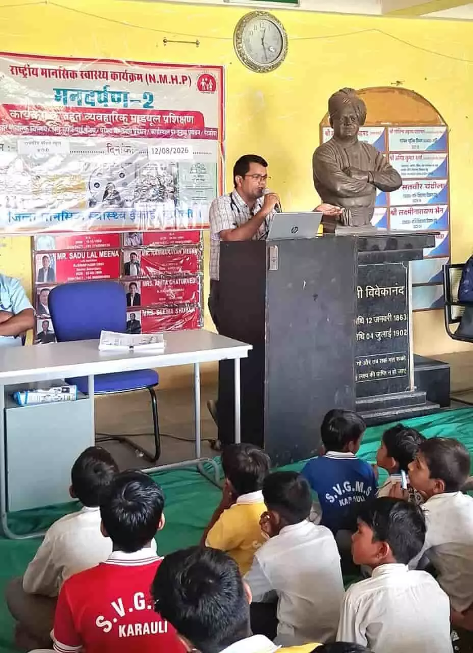 तस्वीर में एक वक्ता मंच पर बोल रहा है और सामने बच्चे बैठे हैं। तस्वीर में एक वक्ता मंच पर बोल रहा है और सामने बच्चे बैठे हैं।