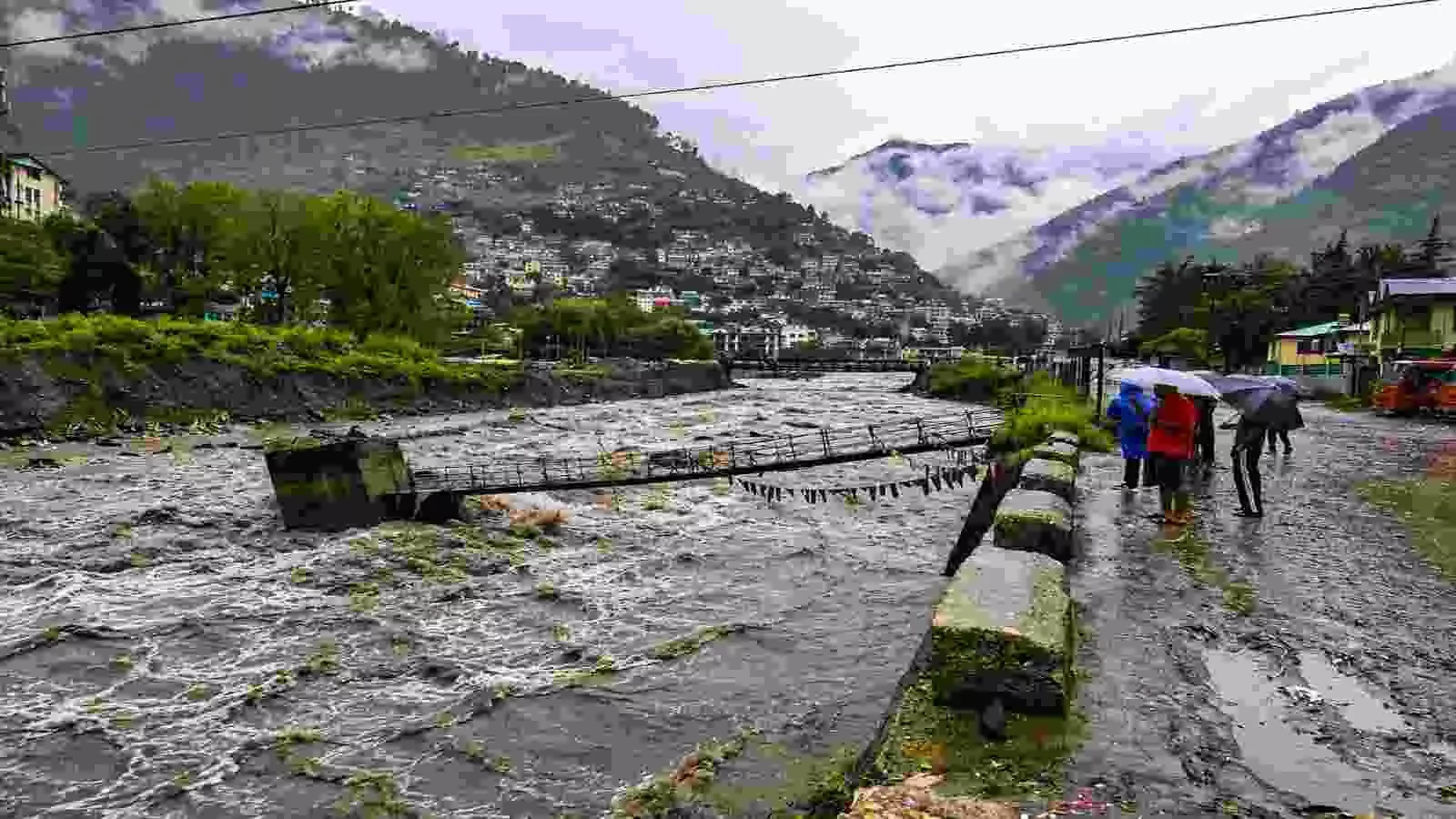 उफान पर बहती नदी और किनारे खड़े लोग हिमाचल और उत्तराखंड में भारी बारिश के संदर्भ में। उफान पर बहती नदी और किनारे खड़े लोग हिमाचल और उत्तराखंड में भारी बारिश के संदर्भ में।