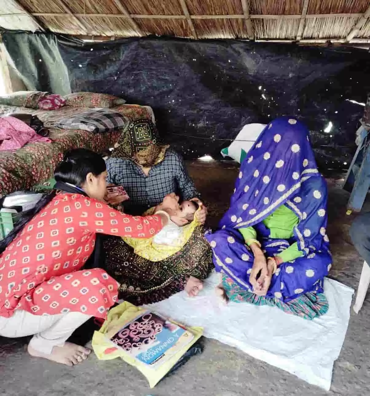 तस्वीर में स्वास्थ्यकर्मी बच्चे को टीका लगाते हुए और महिलाएं बैठी हुई दिखाई दे रही हैं। तस्वीर में स्वास्थ्यकर्मी बच्चे को टीका लगाते हुए और महिलाएं बैठी हुई दिखाई दे रही हैं।