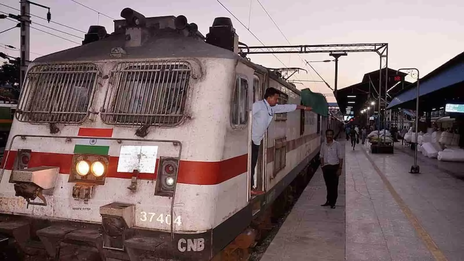 रेलवे स्टेशन पर ट्रेन के इंजन से हरी झंडी दिखाते कर्मी और प्लेटफॉर्म पर खड़े व्यक्ति। रेलवे स्टेशन पर ट्रेन के इंजन से हरी झंडी दिखाते कर्मी और प्लेटफॉर्म पर खड़े व्यक्ति।