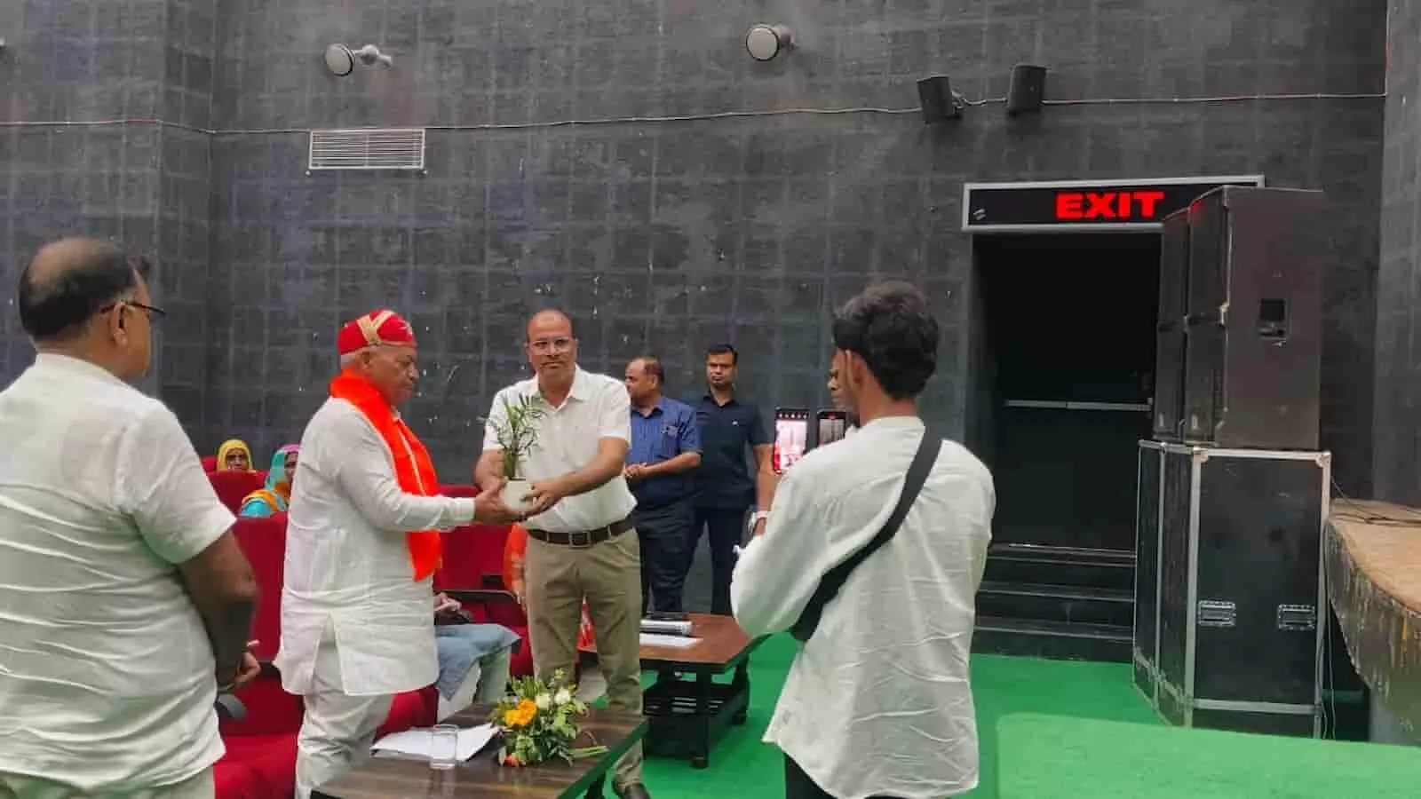 तस्वीर में टाउन हॉल के भीतर अतिथि एक व्यक्ति को पौधा भेंट कर रहे हैं। तस्वीर में टाउन हॉल के भीतर अतिथि एक व्यक्ति को पौधा भेंट कर रहे हैं।