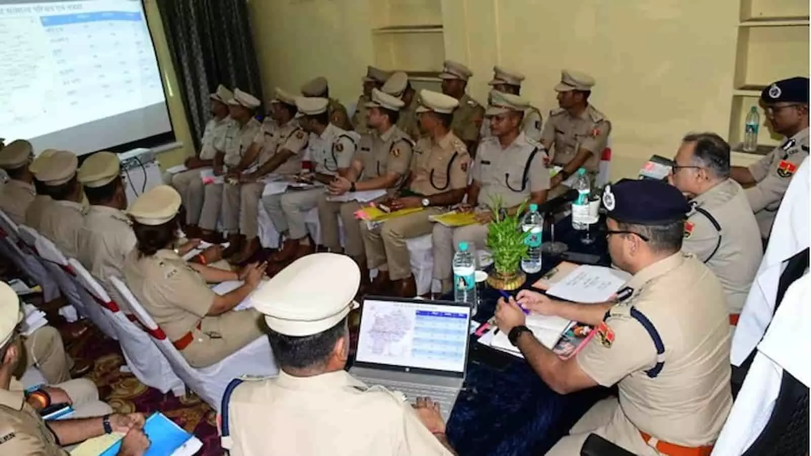 एक कमरे में कई पुलिस अधिकारी कुर्सियों पर बैठकर प्रोजेक्टर स्क्रीन पर प्रस्तुति देखते हुए। एक कमरे में कई पुलिस अधिकारी कुर्सियों पर बैठकर प्रोजेक्टर स्क्रीन पर प्रस्तुति देखते हुए।