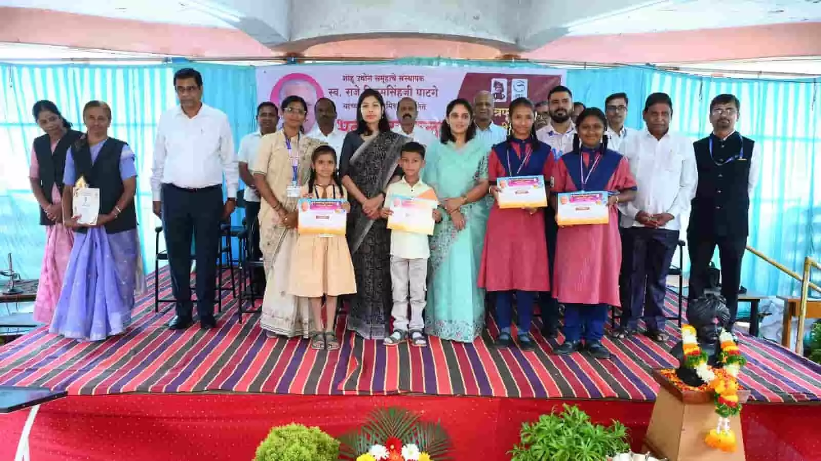 तस्वीर में मंच पर खड़े विजेता विद्यार्थियों और अतिथियों को कोल्हापुर में पुरस्कार वितरण समारोह के दौरान देखा जा सकता है। तस्वीर में मंच पर खड़े विजेता विद्यार्थियों और अतिथियों को कोल्हापुर में पुरस्कार वितरण समारोह के दौरान देखा जा सकता है।