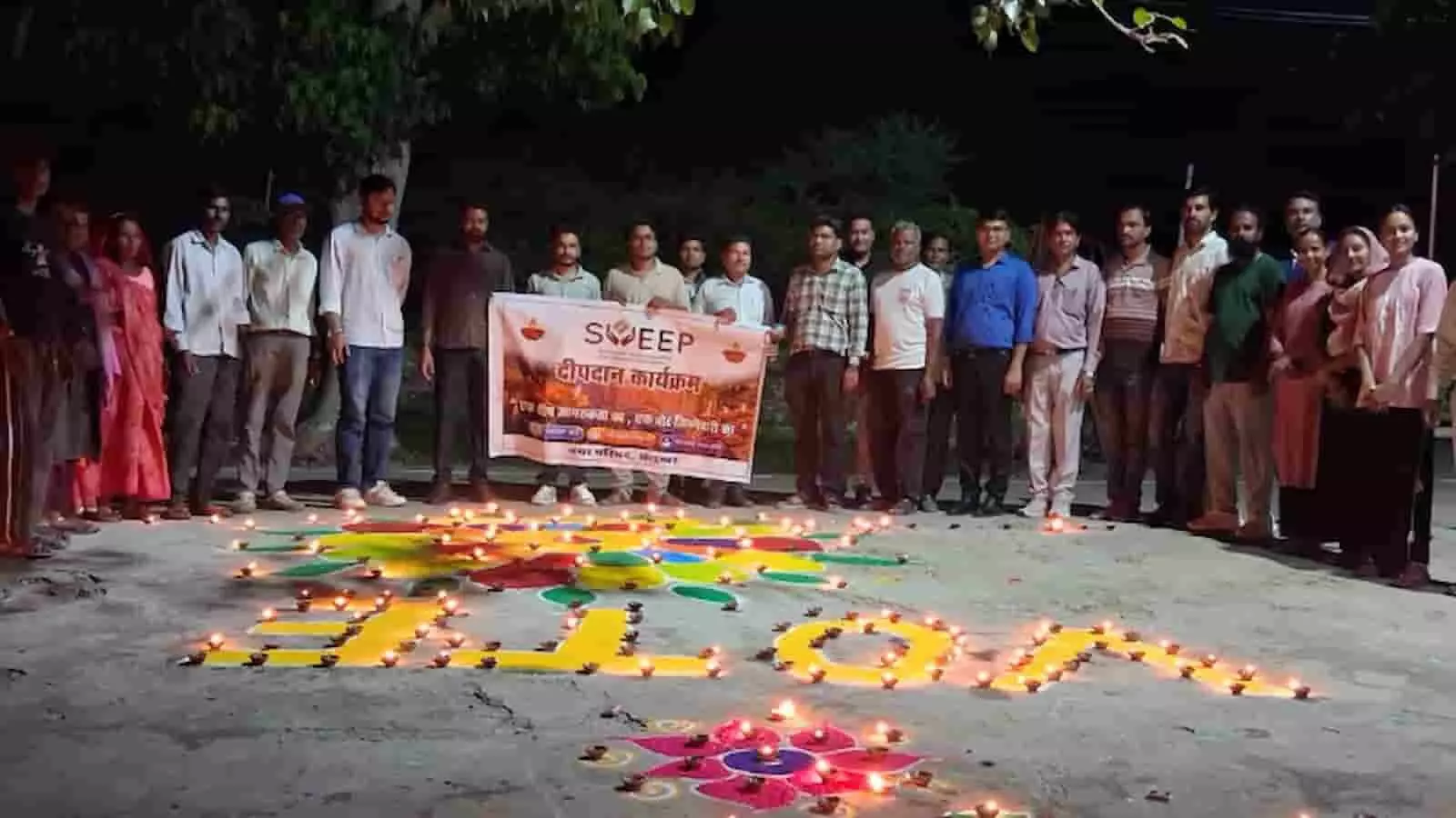 तस्वीर में लोग बैनर के साथ खड़े हैं और जमीन पर दीये व रंगोली सजी है। तस्वीर में लोग बैनर के साथ खड़े हैं और जमीन पर दीये व रंगोली सजी है।