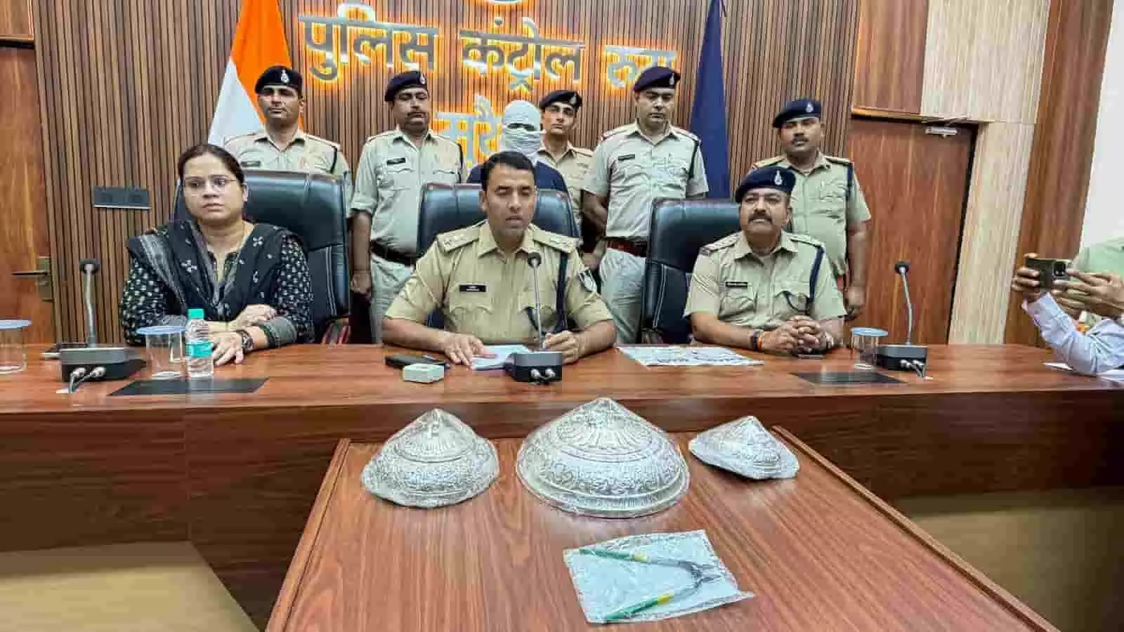 तस्वीर में पुलिस अधिकारियों के साथ पकड़ा गया आरोपी और मेज पर रखी चांदी की वस्तुएं दिख रही हैं। तस्वीर में पुलिस अधिकारियों के साथ पकड़ा गया आरोपी और मेज पर रखी चांदी की वस्तुएं दिख रही हैं।