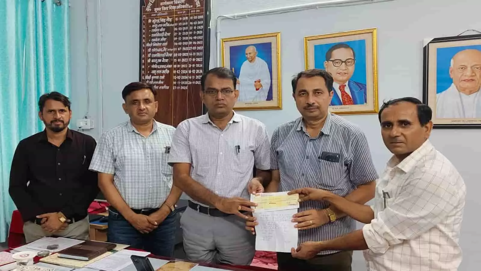 कार्यालय में पांच व्यक्ति एक चेक और दस्तावेज सौंपते हुए दिखाई दे रहे हैं। कार्यालय में पांच व्यक्ति एक चेक और दस्तावेज सौंपते हुए दिखाई दे रहे हैं।