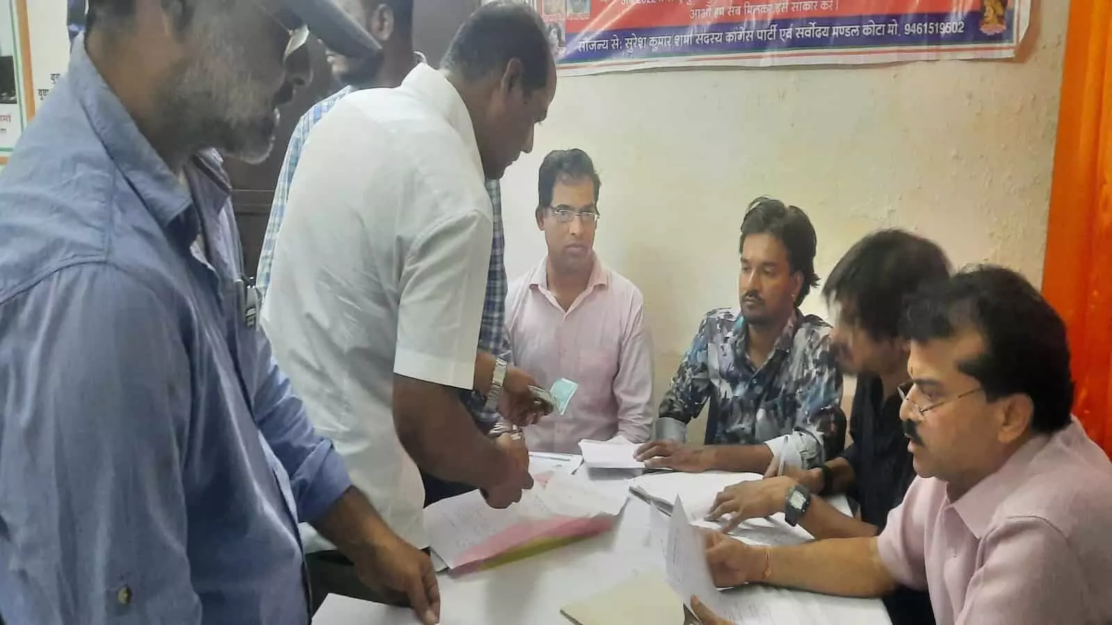 तस्वीर में कोटा कांग्रेस कार्यालय में मेज पर बैठकर चुनावी आवेदन प्रक्रिया पूरी करते लोग। तस्वीर में कोटा कांग्रेस कार्यालय में मेज पर बैठकर चुनावी आवेदन प्रक्रिया पूरी करते लोग।