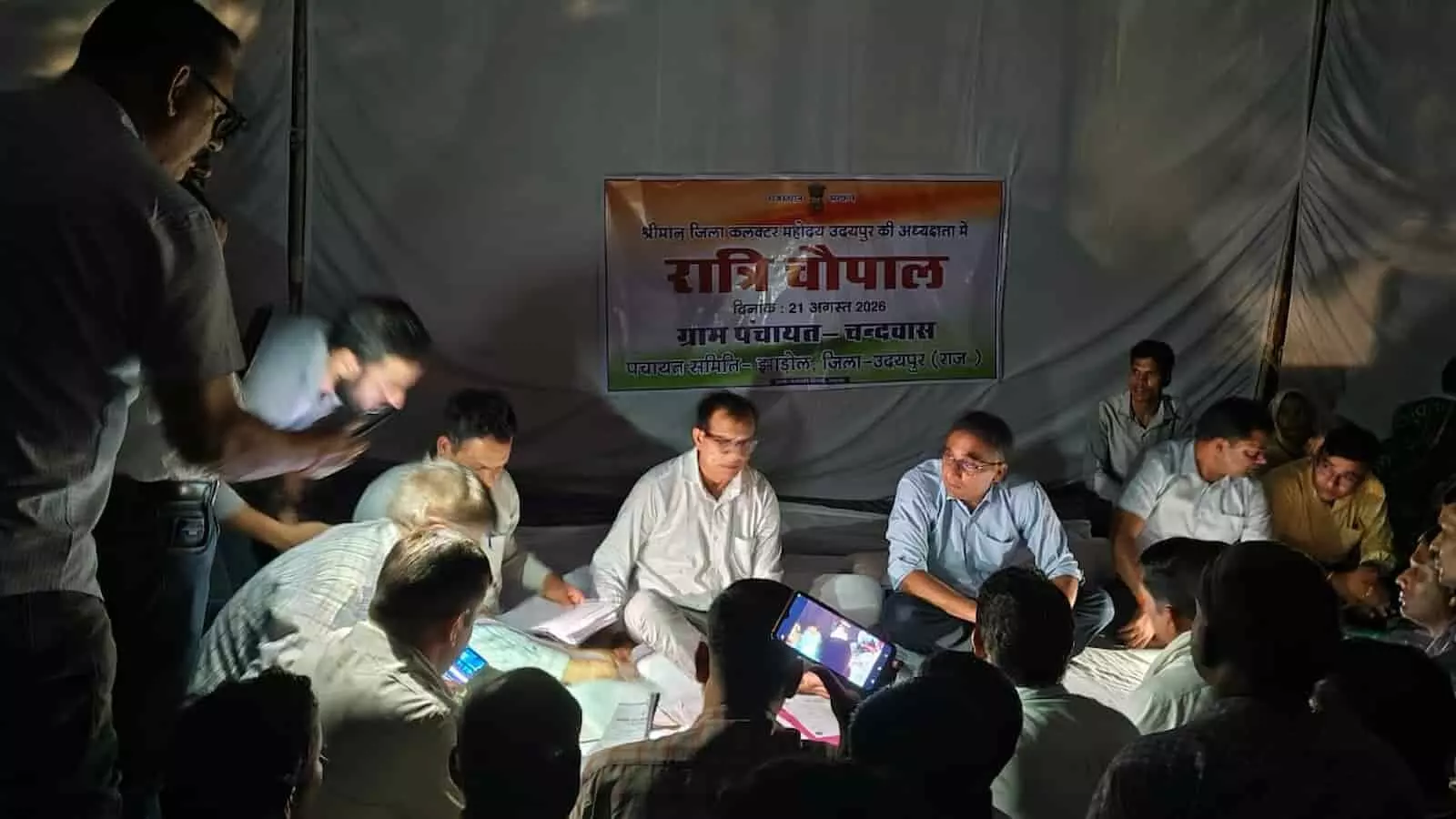 रात्रि चौपाल में अंधेरे के बीच बैठे अधिकारी और ग्रामीण। रात्रि चौपाल में अंधेरे के बीच बैठे अधिकारी और ग्रामीण।