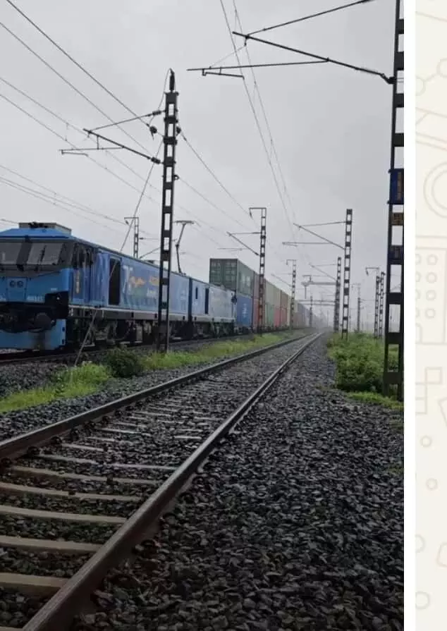 तस्वीर में रेलवे ट्रैक पर चलती हुई डबल-स्टैक कंटेनर ट्रेन और नीला इंजन दिखाई दे रहा है। तस्वीर में रेलवे ट्रैक पर चलती हुई डबल-स्टैक कंटेनर ट्रेन और नीला इंजन दिखाई दे रहा है।