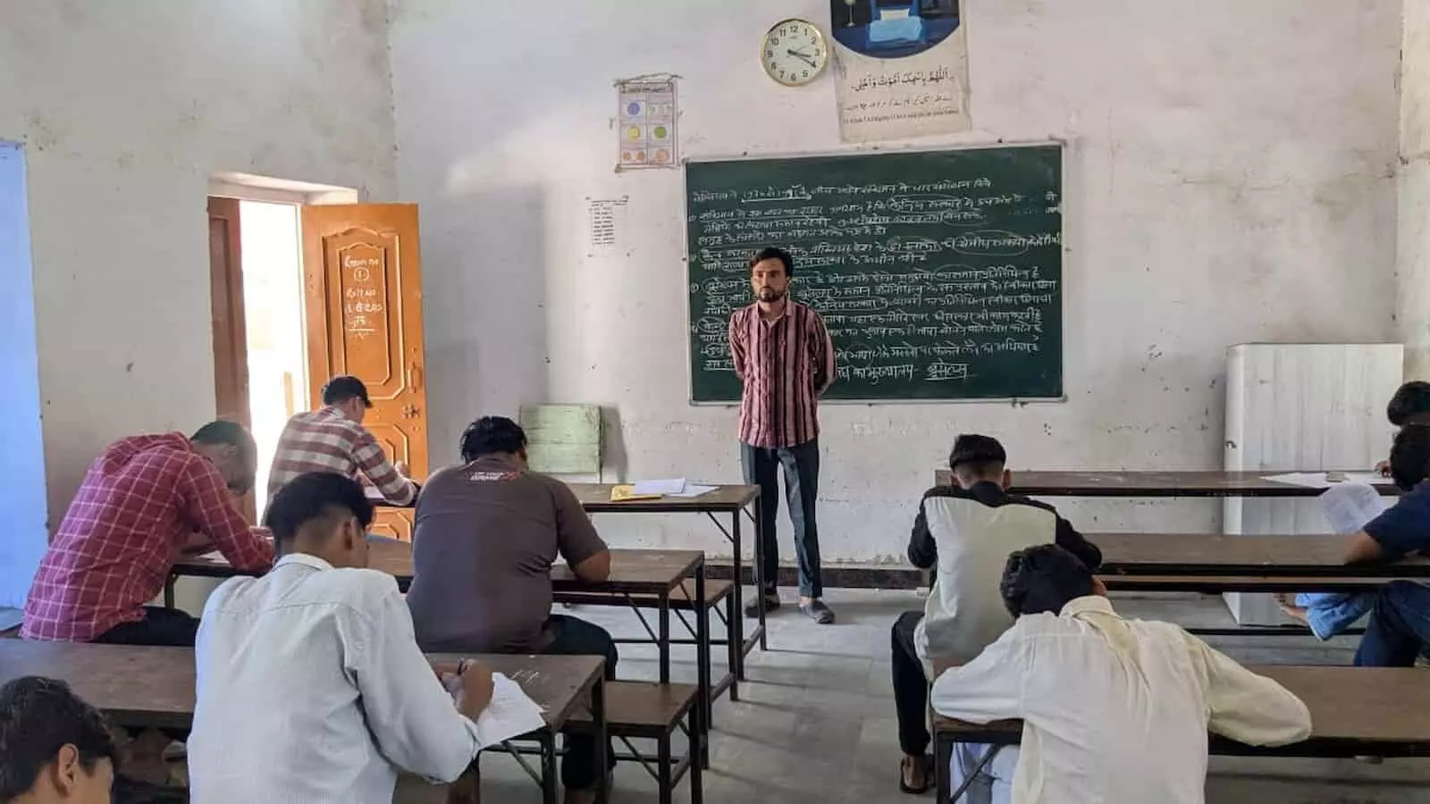 वजीरपुर के परीक्षा हॉल में बेंचों पर बैठकर परीक्षा देते हुए विद्यार्थी और आयोजक नजर आ रहे हैं। वजीरपुर के परीक्षा हॉल में बेंचों पर बैठकर परीक्षा देते हुए विद्यार्थी और आयोजक नजर आ रहे हैं।