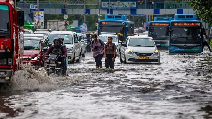 दिल्ली में जलभराव वाले रास्ते से गुजरते वाहन और पैदल यात्री। दिल्ली में जलभराव वाले रास्ते से गुजरते वाहन और पैदल यात्री।