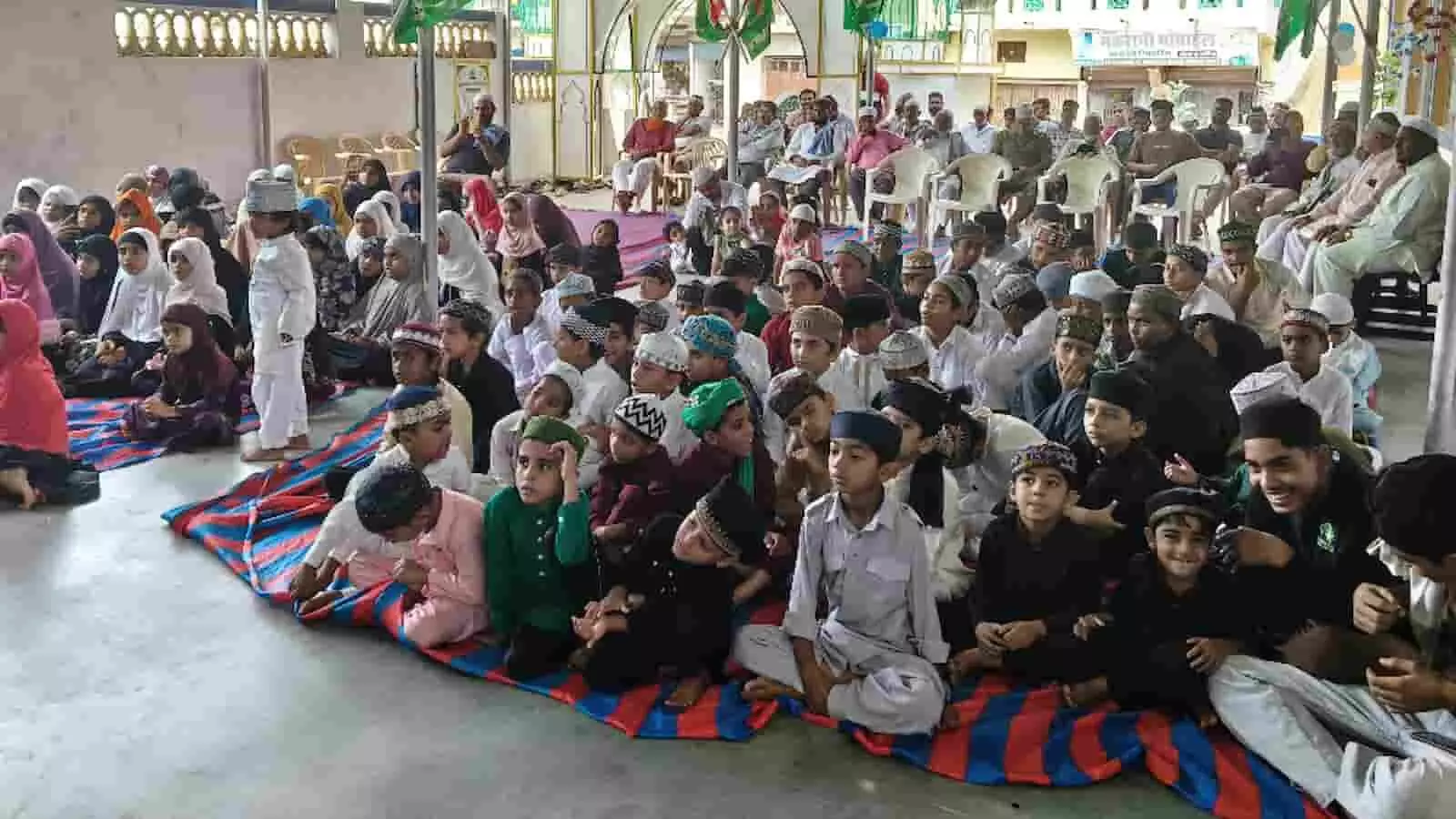 तस्वीर में मदरसा परिसर में फर्श पर बैठे बच्चे और पीछे कुर्सियों पर बैठे लोग नजर आ रहे हैं। तस्वीर में मदरसा परिसर में फर्श पर बैठे बच्चे और पीछे कुर्सियों पर बैठे लोग नजर आ रहे हैं।