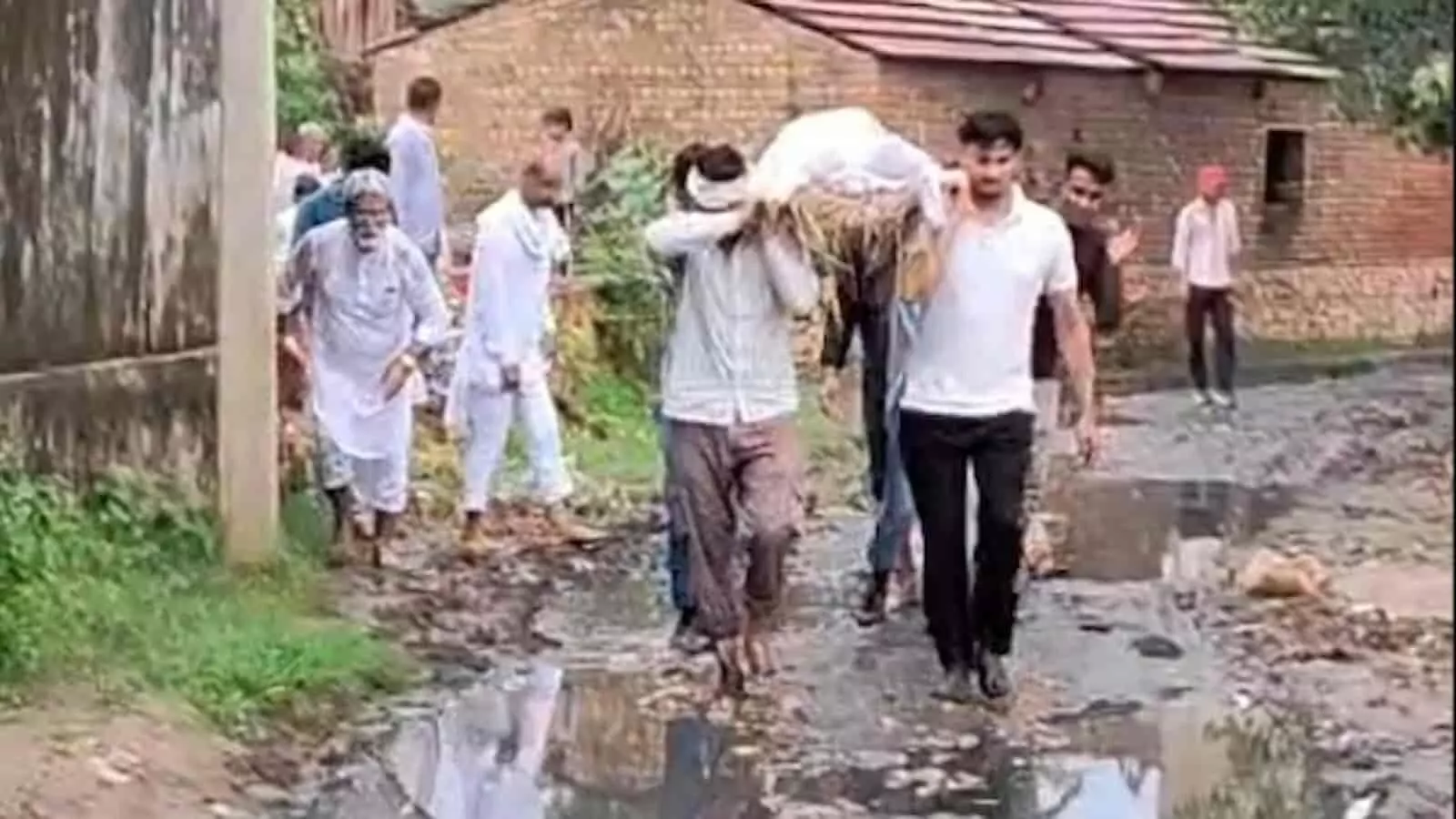 तस्वीर में ग्रामीण नरहरपुर गांव के कीचड़युक्त और जलभराव वाले रास्ते से शव यात्रा निकालते दिख रहे हैं। तस्वीर में ग्रामीण नरहरपुर गांव के कीचड़युक्त और जलभराव वाले रास्ते से शव यात्रा निकालते दिख रहे हैं।
