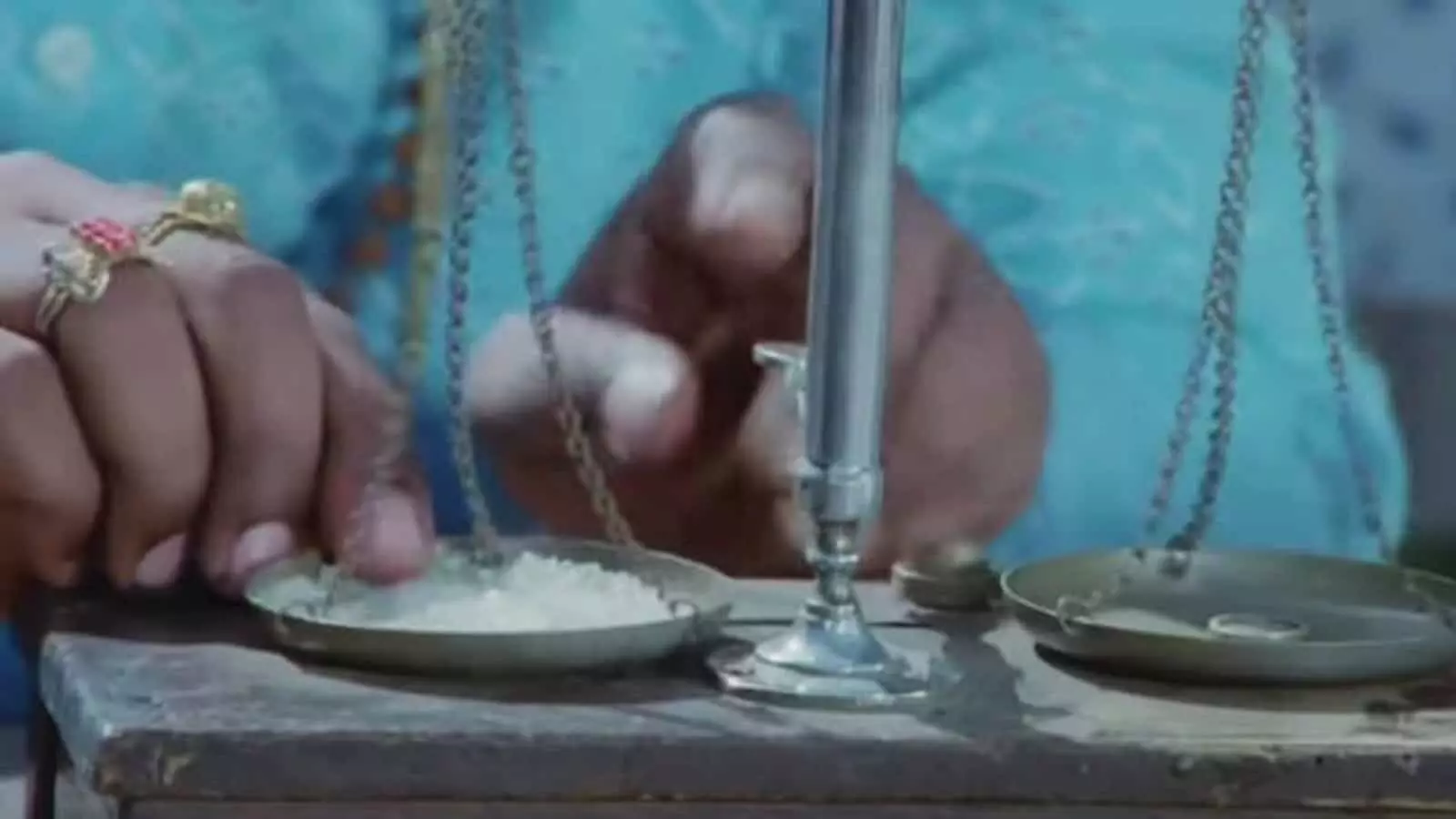 तराजूत साखर तोलताना दिसणारा एक व्यक्ती दुकान परिसरामध्ये बसलेला आहे तराजूत साखर तोलताना दिसणारा एक व्यक्ती दुकान परिसरामध्ये बसलेला आहे