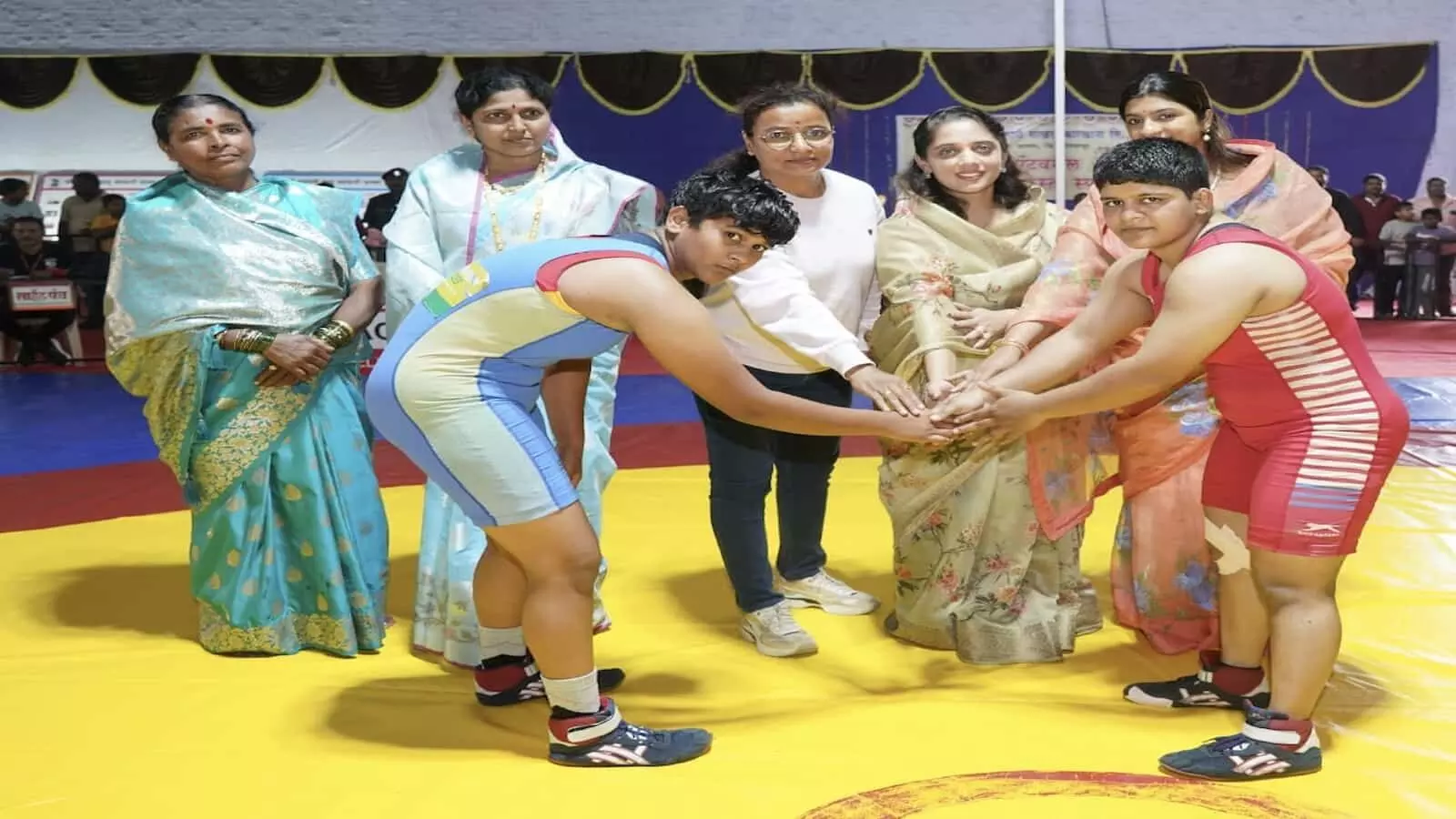इनडोर हॉल में कुश्ती मैट पर अतिथियों के साथ हाथ मिलाती दो महिला पहलवान। इनडोर हॉल में कुश्ती मैट पर अतिथियों के साथ हाथ मिलाती दो महिला पहलवान।
