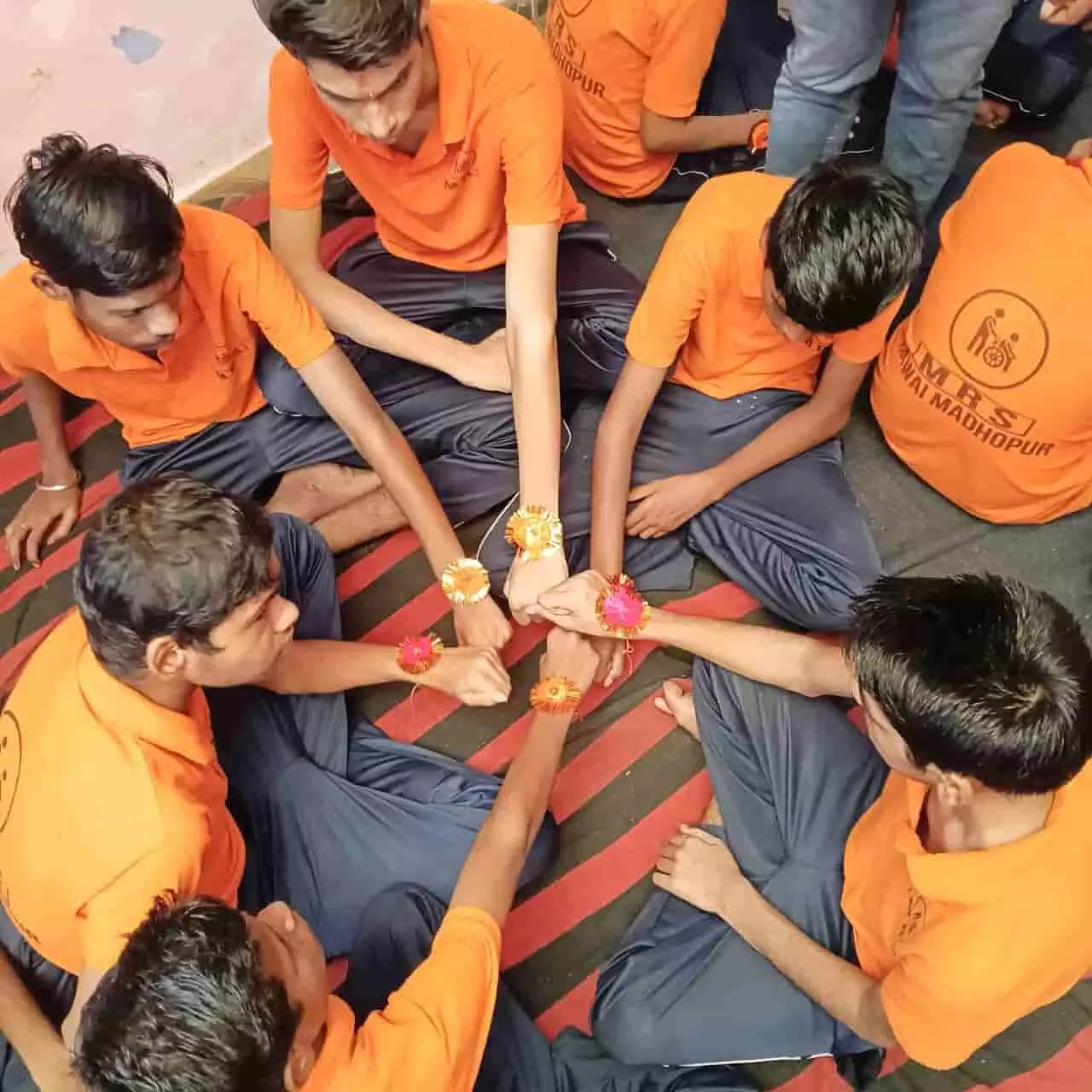 तस्वीर में नारंगी पोशाक पहने दिव्यांग छात्र अपनी कलाइयों पर बंधी राखियां दिखाते हुए। तस्वीर में नारंगी पोशाक पहने दिव्यांग छात्र अपनी कलाइयों पर बंधी राखियां दिखाते हुए।