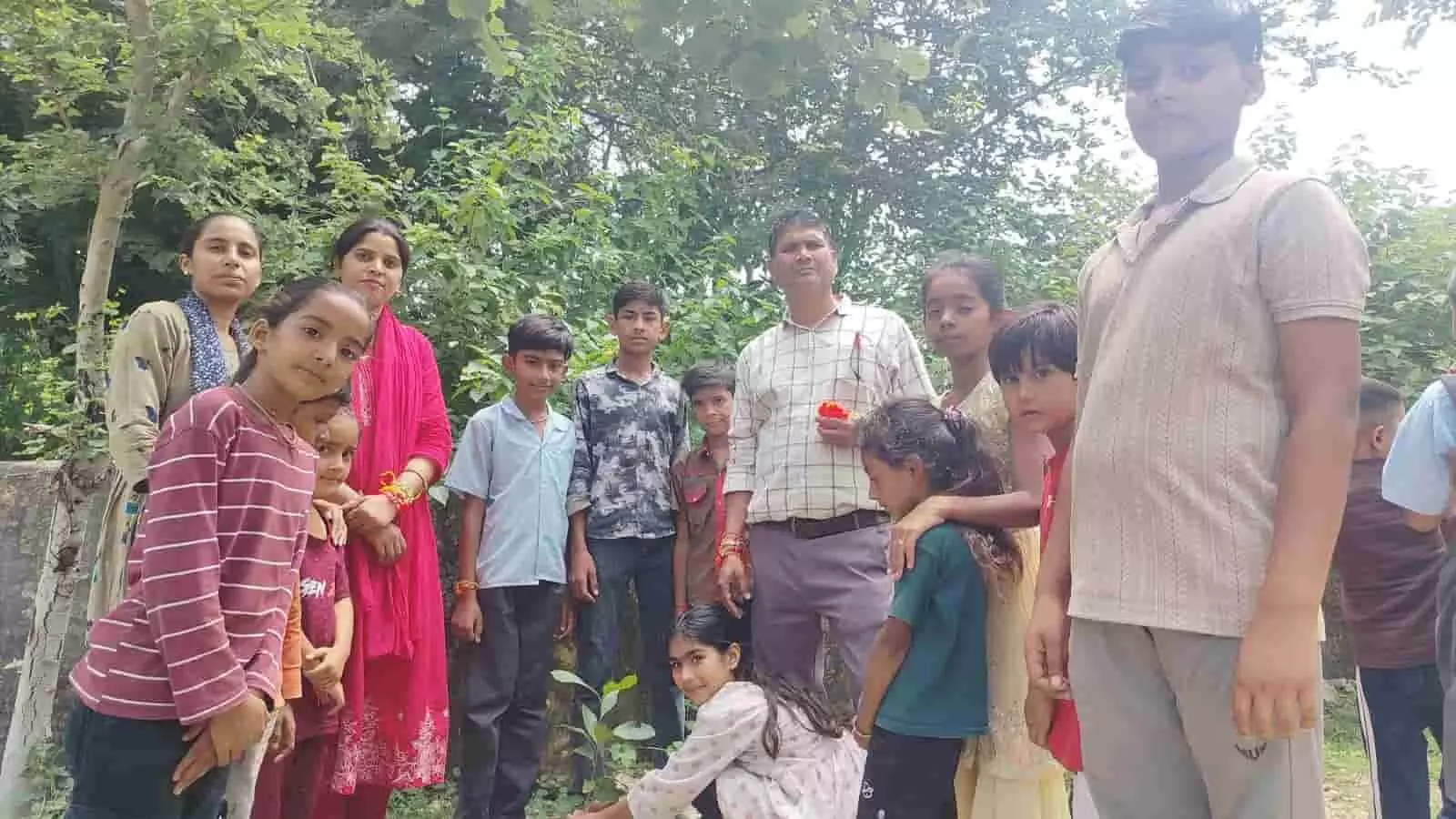 ढणा गांव के विद्यालय में पौधे के पास खड़े विद्यार्थी और शिक्षक ढणा गांव के विद्यालय में पौधे के पास खड़े विद्यार्थी और शिक्षक