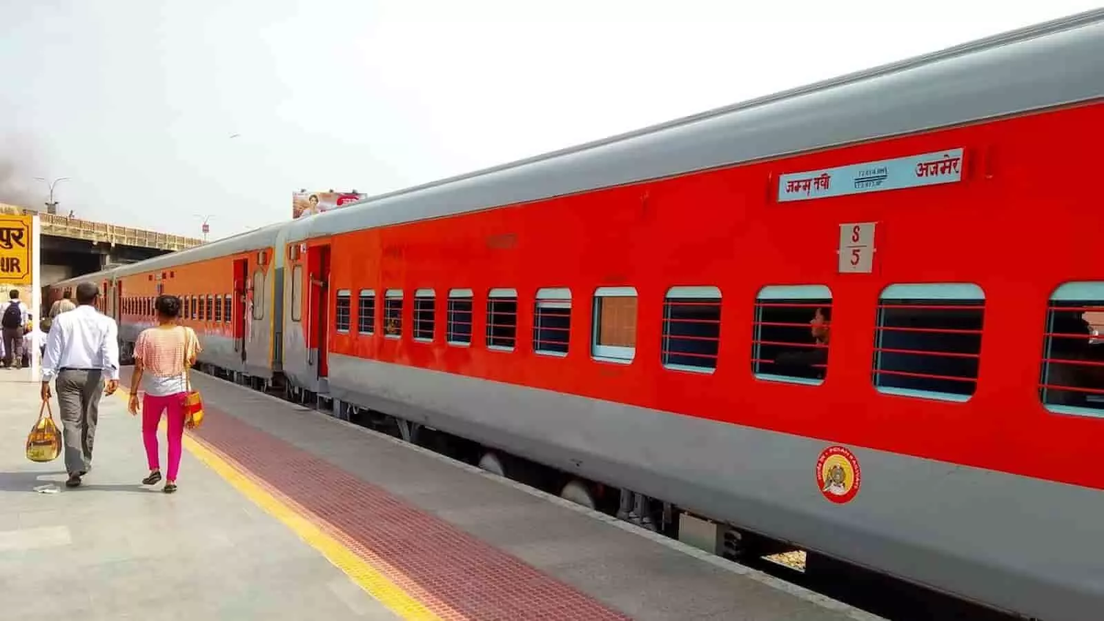 तस्वीर में रेलवे स्टेशन पर ट्रेन और प्लेटफॉर्म पर चलते हुए यात्री दिख रहे हैं। तस्वीर में रेलवे स्टेशन पर ट्रेन और प्लेटफॉर्म पर चलते हुए यात्री दिख रहे हैं।