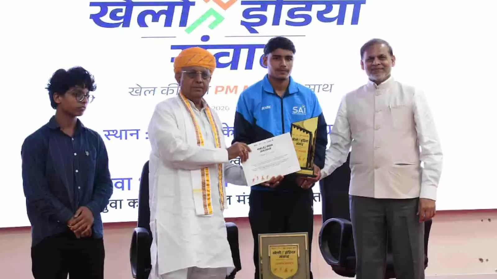 खेलो इंडिया संवाद कार्यक्रम के दौरान अतिथियों द्वारा युवा एथलीट को सम्मानित करते हुए तस्वीर में देखा जा सकता है। खेलो इंडिया संवाद कार्यक्रम के दौरान अतिथियों द्वारा युवा एथलीट को सम्मानित करते हुए तस्वीर में देखा जा सकता है।