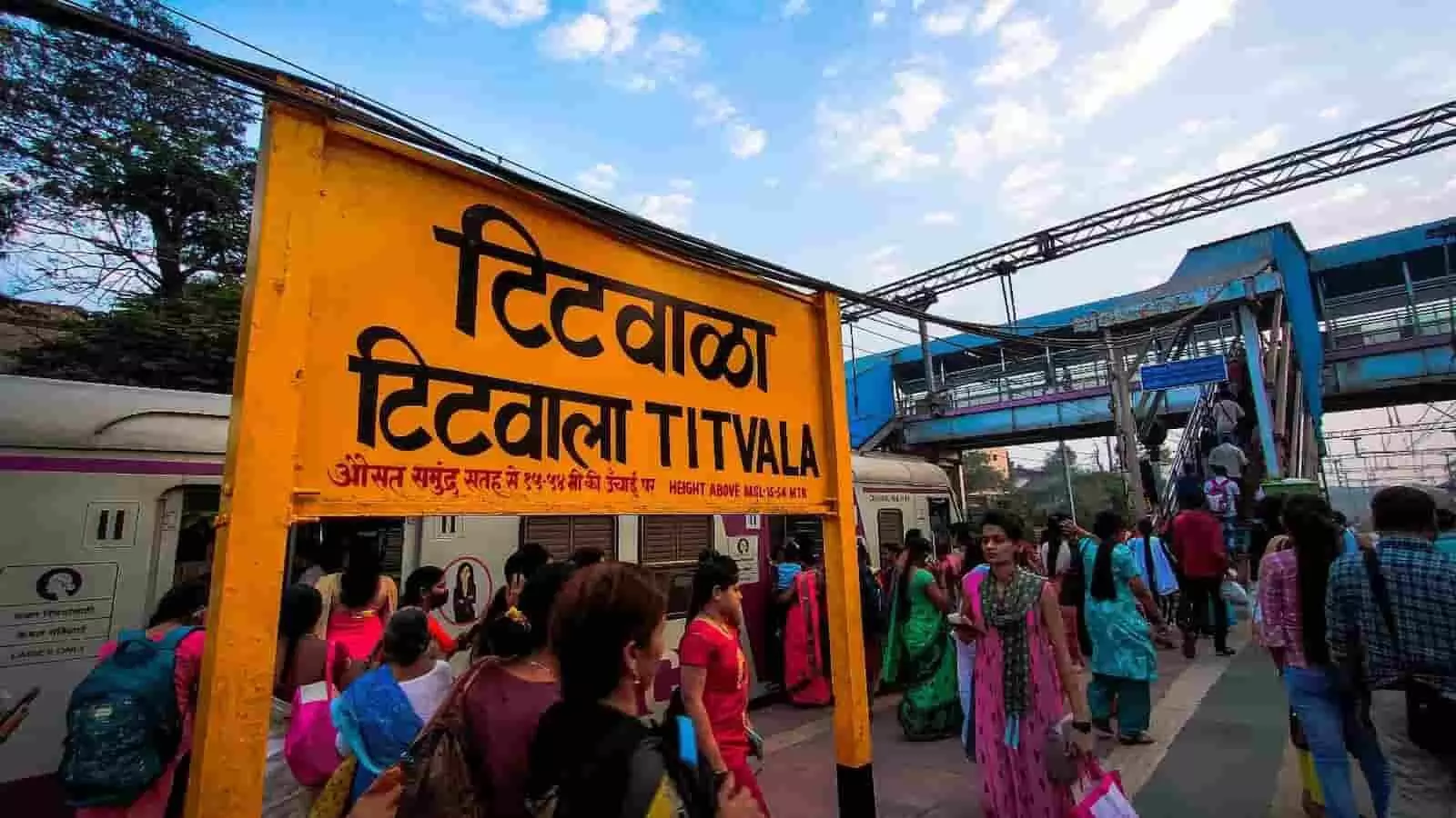 टिटवाला रेलवे स्टेशन के प्लेटफॉर्म पर यात्रियों की भीड़ और स्टेशन का पीला बोर्ड। टिटवाला रेलवे स्टेशन के प्लेटफॉर्म पर यात्रियों की भीड़ और स्टेशन का पीला बोर्ड।