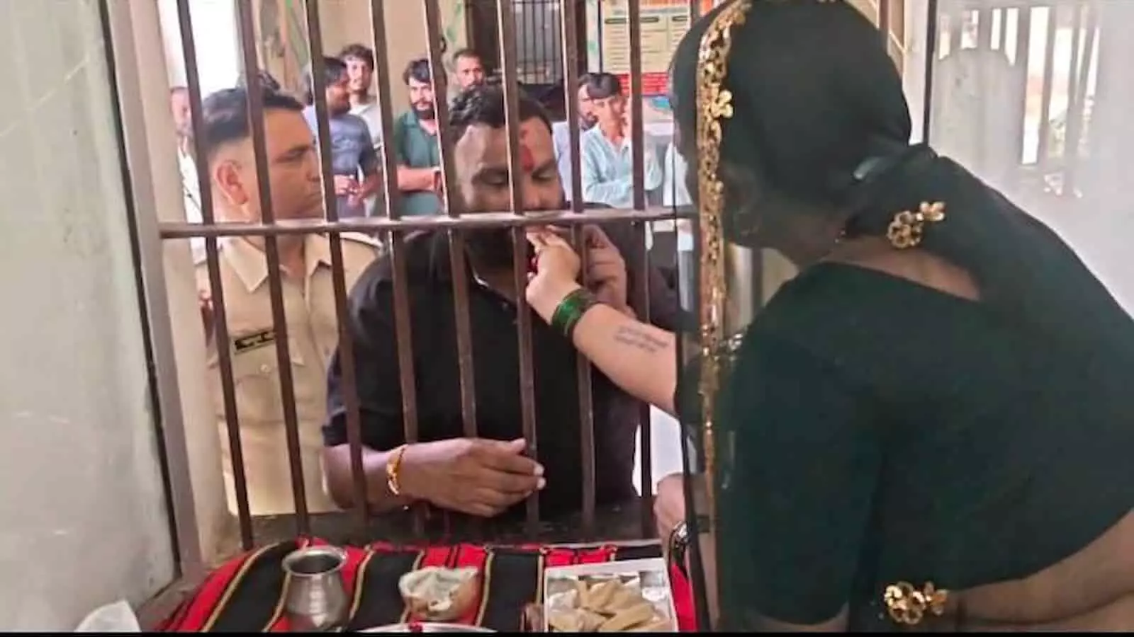 तस्वीर में एक महिला जिला जेल की सलाखों के पीछे खड़े बंदी को राखी बांध रही है. तस्वीर में एक महिला जिला जेल की सलाखों के पीछे खड़े बंदी को राखी बांध रही है.
