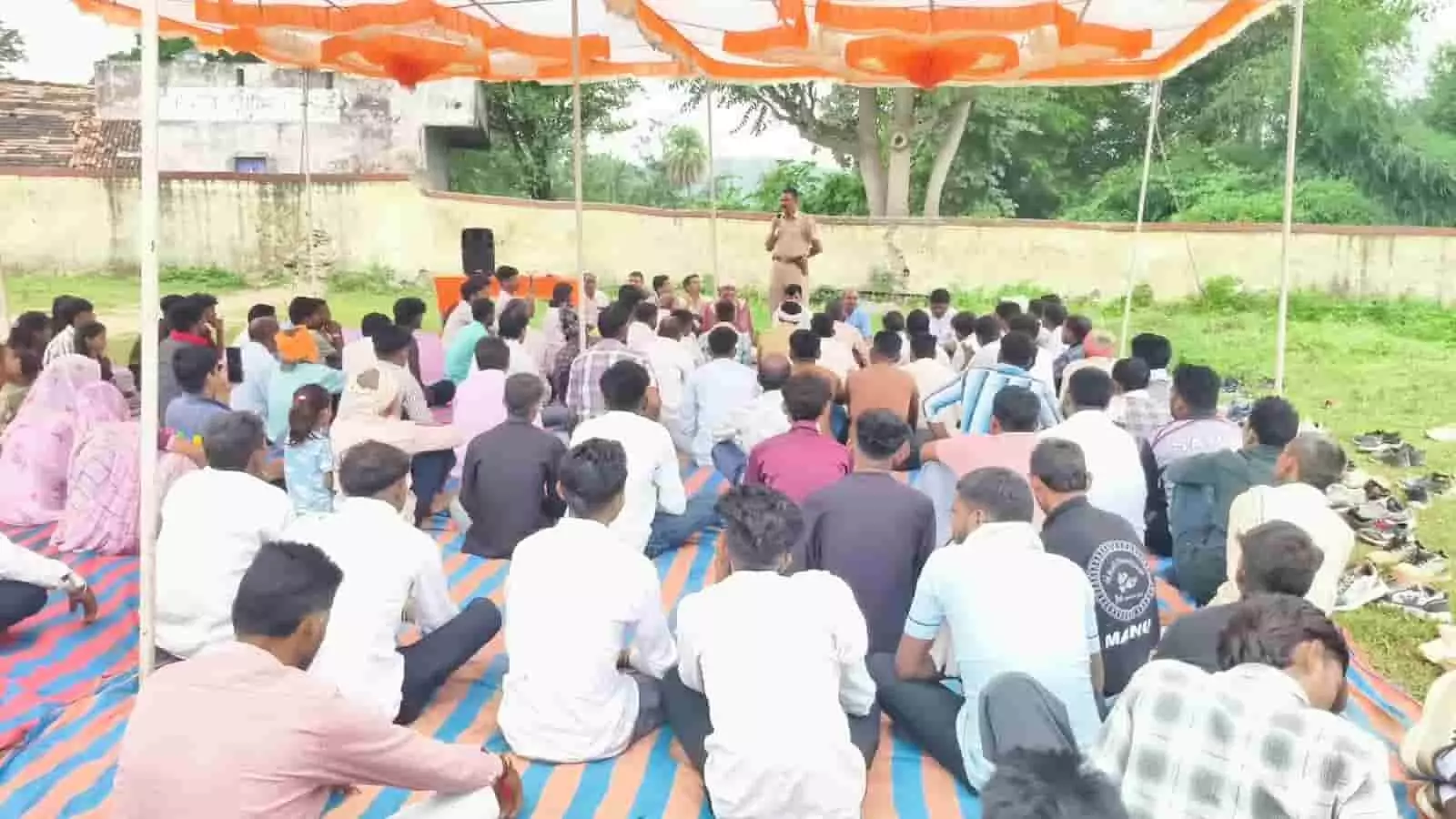 तस्वीर में बावलवाड़ा में लोग बैठे हैं, एक पुलिसकर्मी संबोधित कर रहा है। तस्वीर में बावलवाड़ा में लोग बैठे हैं, एक पुलिसकर्मी संबोधित कर रहा है।