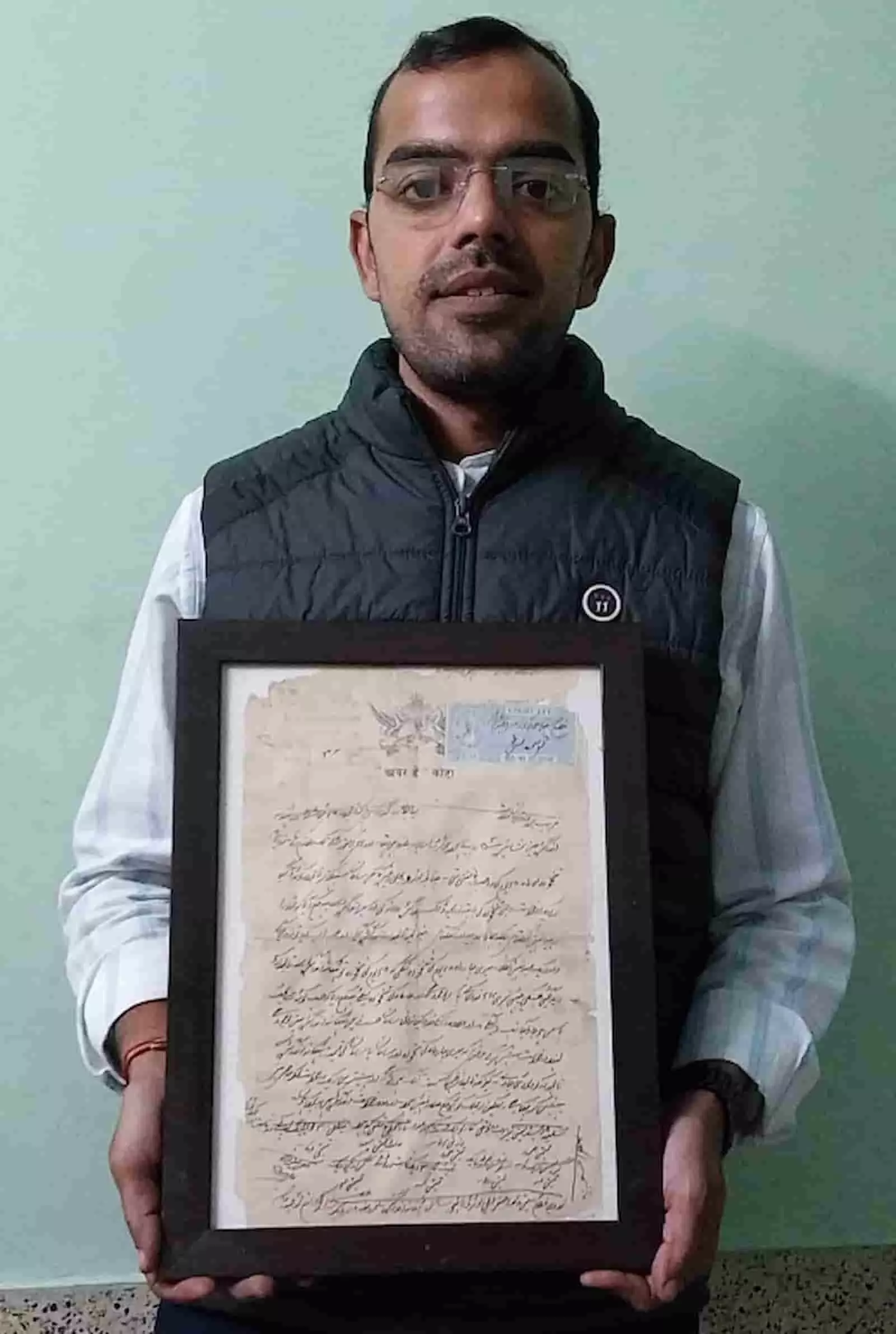 तस्वीर में एक व्यक्ति कोटा में ऐतिहासिक पुराना दस्तावेज फ्रेम में पकड़े हुए खड़ा है। तस्वीर में एक व्यक्ति कोटा में ऐतिहासिक पुराना दस्तावेज फ्रेम में पकड़े हुए खड़ा है।