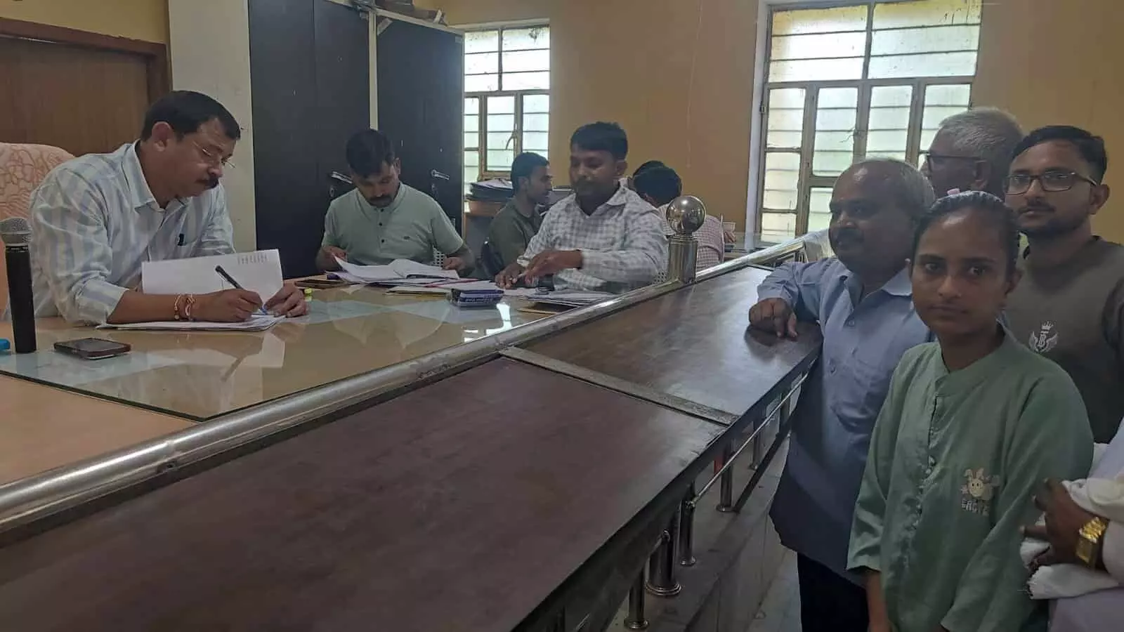 उपखंड अधिकारी कार्यालय के काउंटर पर कागजात जांचते अधिकारी और खड़े लोग। उपखंड अधिकारी कार्यालय के काउंटर पर कागजात जांचते अधिकारी और खड़े लोग।