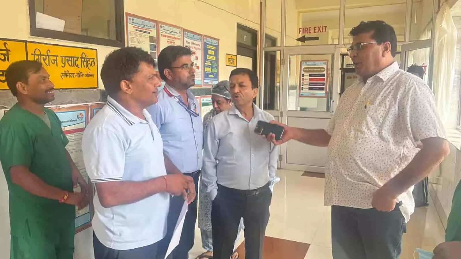 तस्वीर में बाईं से दाईं ओर खड़े स्वास्थ्य कर्मी और अधिकारी अस्पताल के गलियारे में बातचीत कर रहे हैं। तस्वीर में बाईं से दाईं ओर खड़े स्वास्थ्य कर्मी और अधिकारी अस्पताल के गलियारे में बातचीत कर रहे हैं।