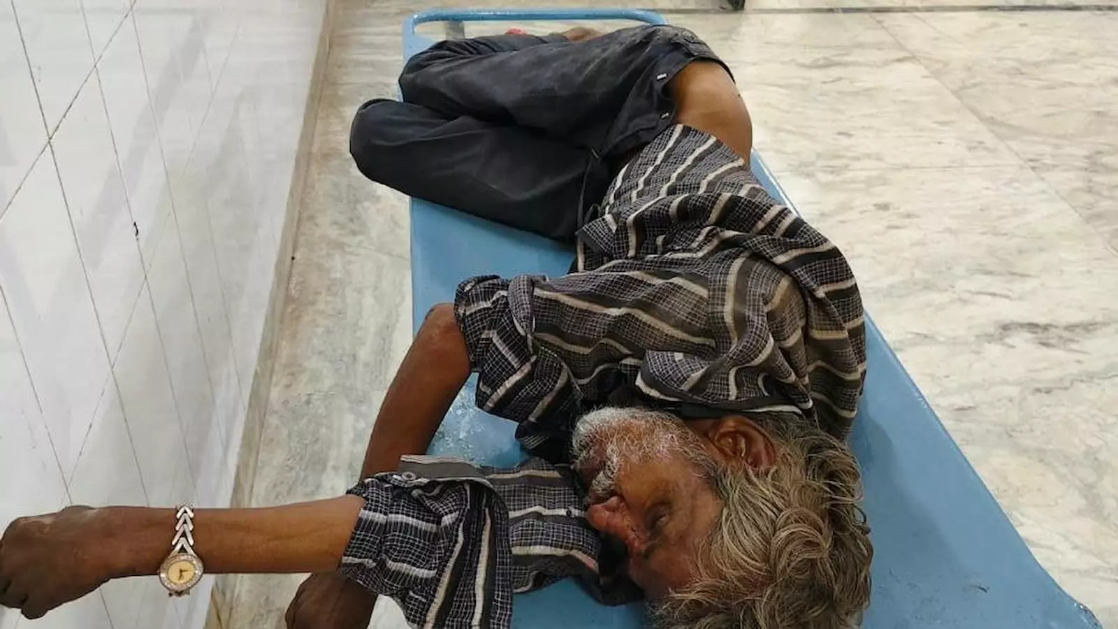 अस्पताल के गलियारे में नीले स्ट्रेचर पर एक अधेड़ व्यक्ति अचेत अवस्था में लेटा हुआ है। अस्पताल के गलियारे में नीले स्ट्रेचर पर एक अधेड़ व्यक्ति अचेत अवस्था में लेटा हुआ है।