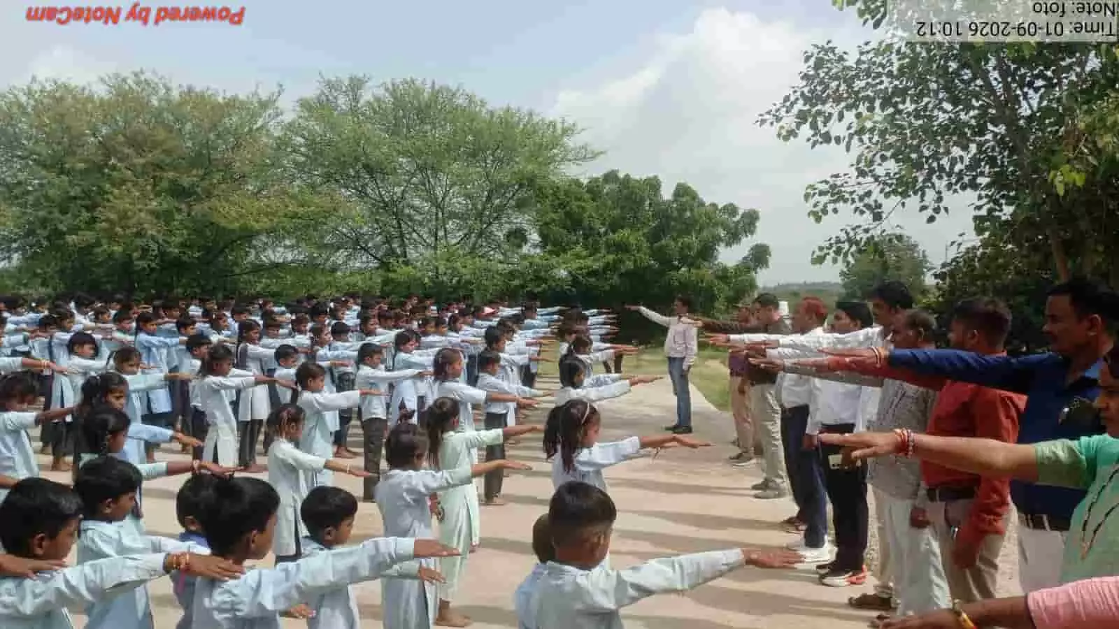तस्वीर में स्कूली छात्र और शिक्षक खुले मैदान में हाथ आगे बढ़ाकर शपथ लेते दिख रहे हैं। तस्वीर में स्कूली छात्र और शिक्षक खुले मैदान में हाथ आगे बढ़ाकर शपथ लेते दिख रहे हैं।