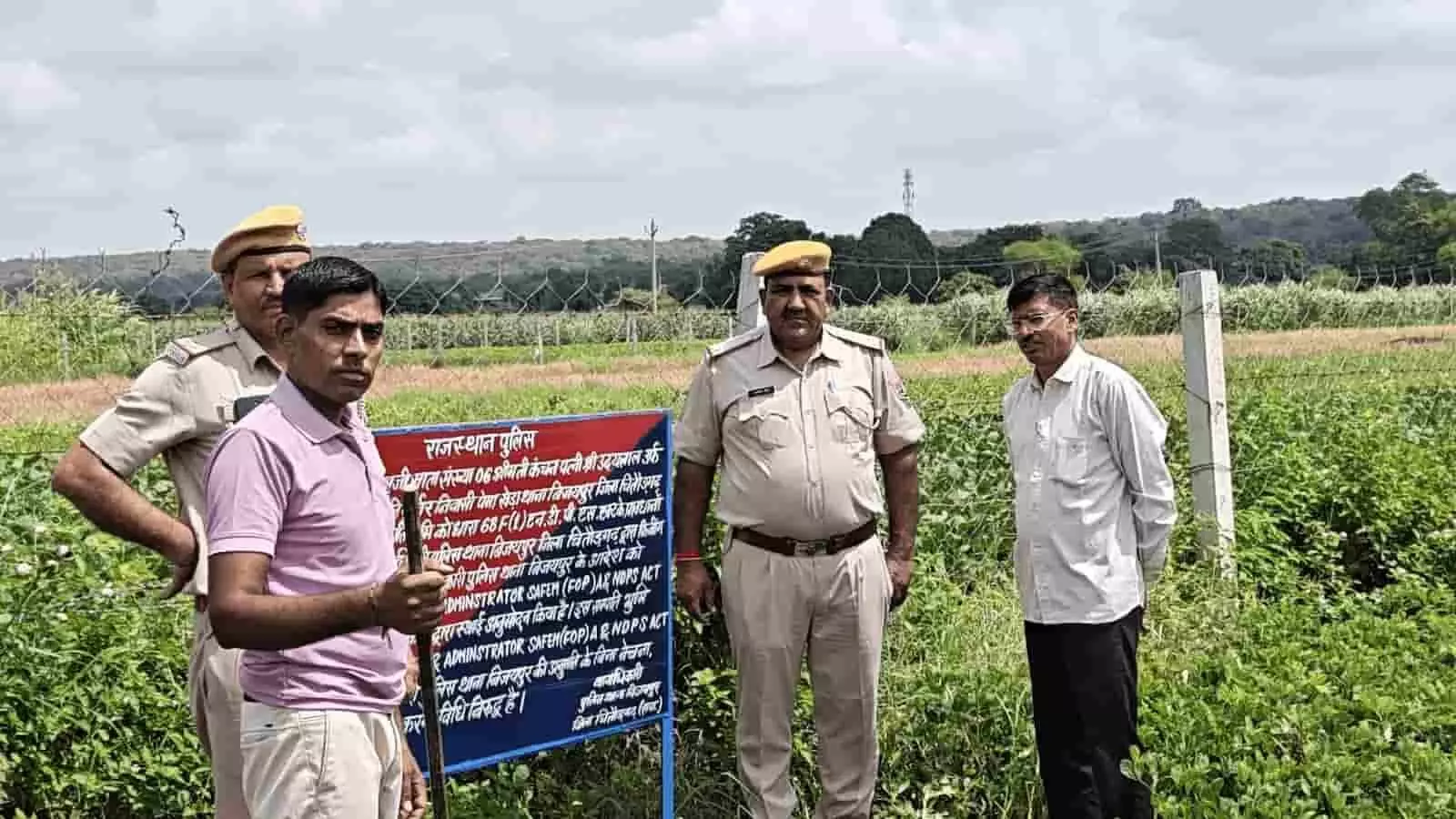 तस्वीर में पुलिसकर्मी और अन्य व्यक्ति चित्तौड़गढ़ में ज़ब्त की गई ज़मीन के बोर्ड के पास खड़े हैं। तस्वीर में पुलिसकर्मी और अन्य व्यक्ति चित्तौड़गढ़ में ज़ब्त की गई ज़मीन के बोर्ड के पास खड़े हैं।