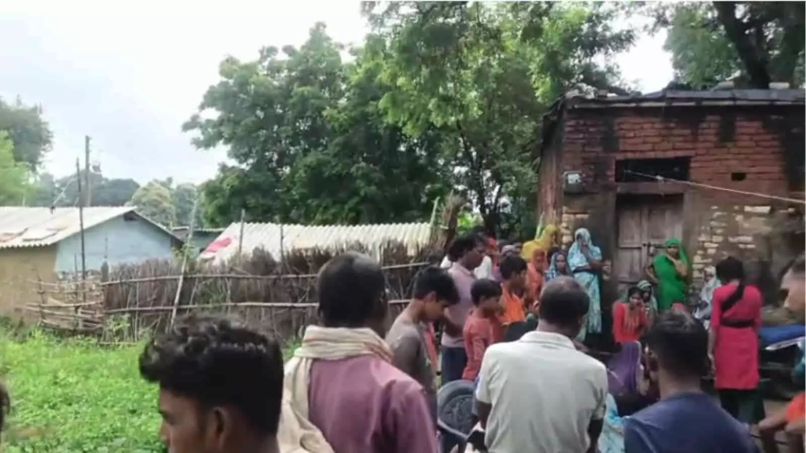 तस्वीर में दिख रही जगह पर ग्रामीण महिलाएं और पुरुष एक ईंट के घर के बाहर खड़े हैं। तस्वीर में दिख रही जगह पर ग्रामीण महिलाएं और पुरुष एक ईंट के घर के बाहर खड़े हैं।