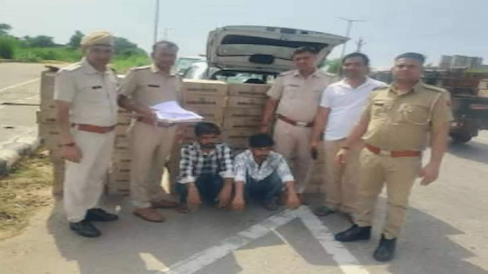 तस्वीर में पुलिसकर्मी और दो गिरफ्तार आरोपी खुली कार और शराब के कार्टूनों के साथ खड़े हैं। तस्वीर में पुलिसकर्मी और दो गिरफ्तार आरोपी खुली कार और शराब के कार्टूनों के साथ खड़े हैं।