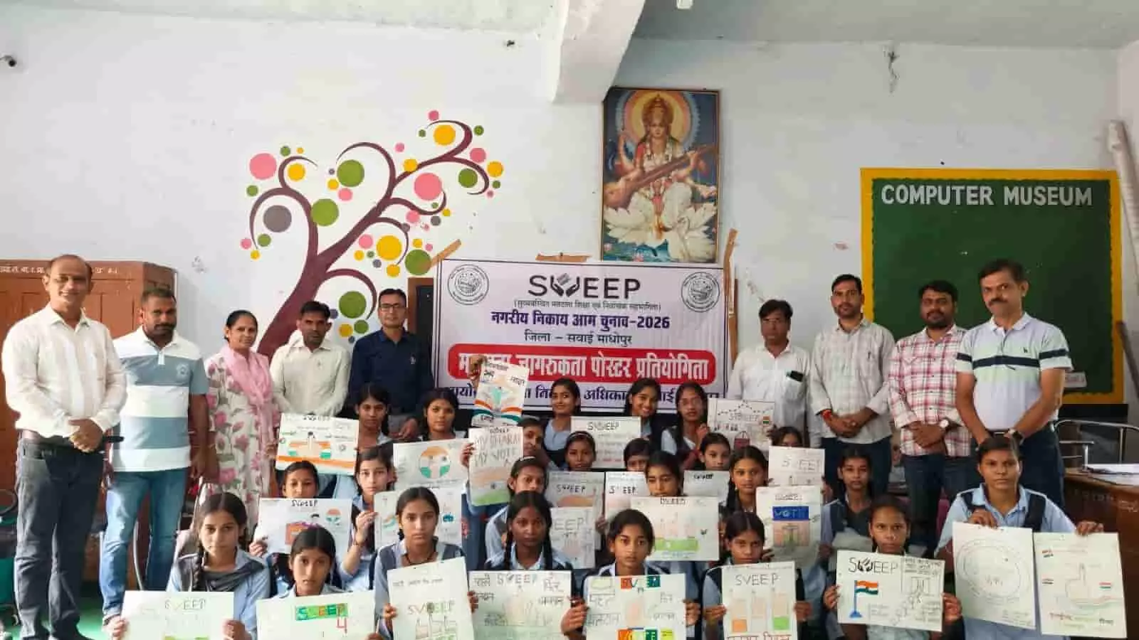 तस्वीर में विद्यार्थी और शिक्षक विद्यालय के कमरे में हाथ में मतदान जागरूकता पोस्टर थामे खड़े और बैठे हैं। तस्वीर में विद्यार्थी और शिक्षक विद्यालय के कमरे में हाथ में मतदान जागरूकता पोस्टर थामे खड़े और बैठे हैं।
