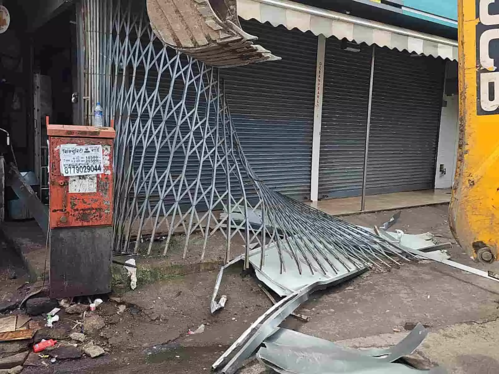 तस्वीर में एक पीली जेसीबी मशीन सड़क किनारे दुकान के शटर को गिरा रही है। तस्वीर में एक पीली जेसीबी मशीन सड़क किनारे दुकान के शटर को गिरा रही है।
