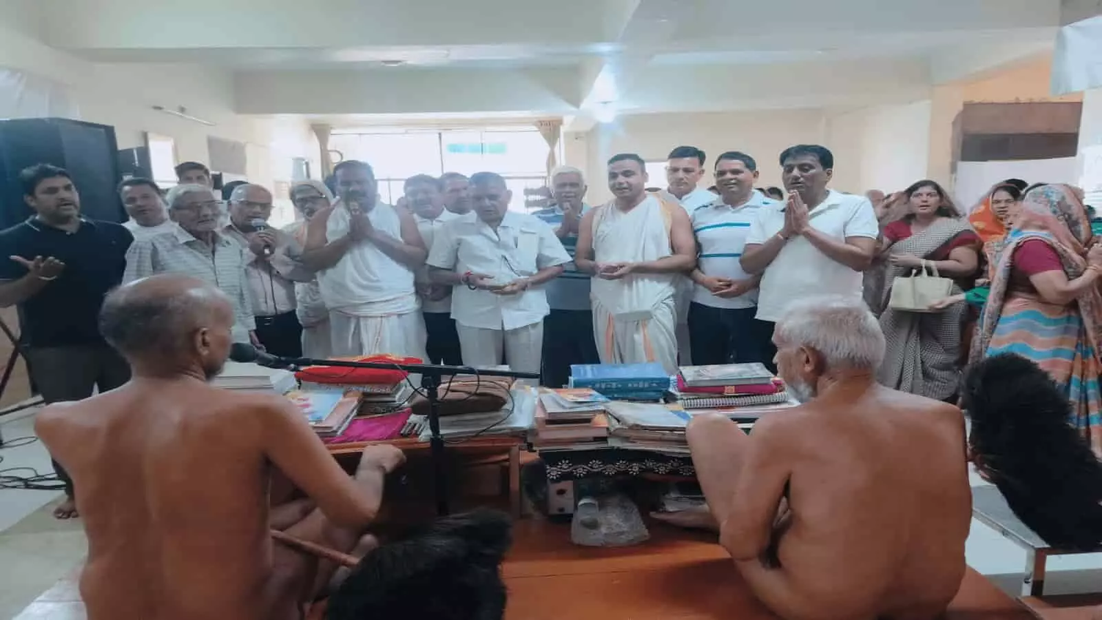 तस्वीर में दो संत मंच पर बैठे हैं और कई लोग सामने खड़े होकर प्रार्थना कर रहे हैं। तस्वीर में दो संत मंच पर बैठे हैं और कई लोग सामने खड़े होकर प्रार्थना कर रहे हैं।