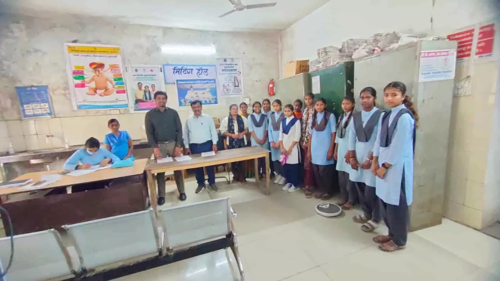 तस्वीर में अस्पताल के कमरे में खड़े मेडिकल स्टाफ, शिक्षक और स्कूली बालिकाएं नजर आ रही हैं। तस्वीर में अस्पताल के कमरे में खड़े मेडिकल स्टाफ, शिक्षक और स्कूली बालिकाएं नजर आ रही हैं।