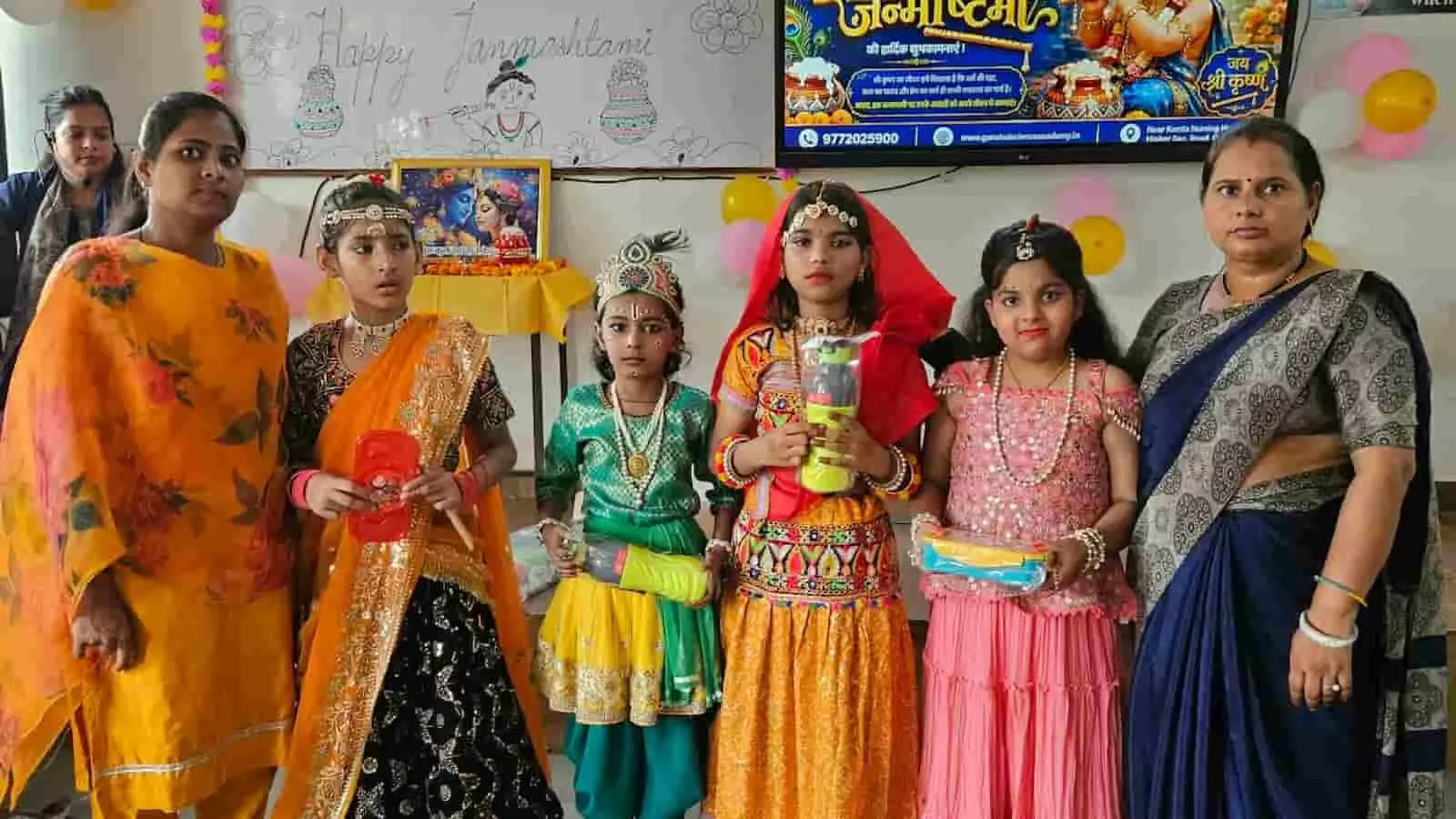 तस्वीर में बाएं से दाएं, शिक्षक, कृष्ण और राधा की वेशभूषा में बच्चे और अन्य शिक्षक स्कूल में खड़े हैं। तस्वीर में बाएं से दाएं, शिक्षक, कृष्ण और राधा की वेशभूषा में बच्चे और अन्य शिक्षक स्कूल में खड़े हैं।