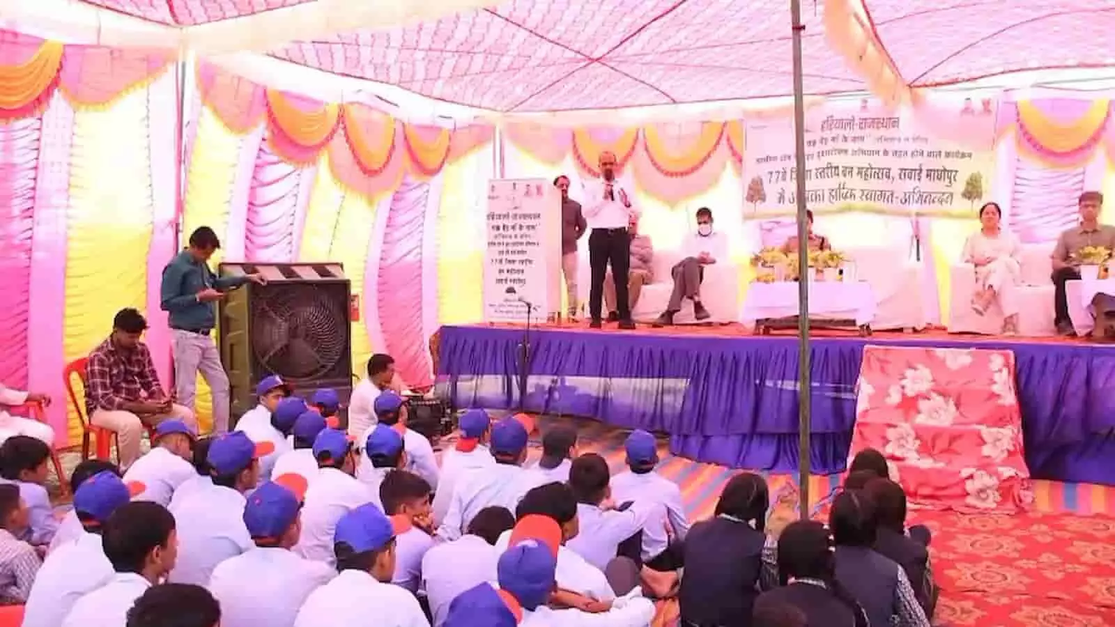तस्वीर में एक अधिकारी मंच से खड़े होकर पंडाल में बैठे लोगों को संबोधित कर रहे हैं। तस्वीर में एक अधिकारी मंच से खड़े होकर पंडाल में बैठे लोगों को संबोधित कर रहे हैं।