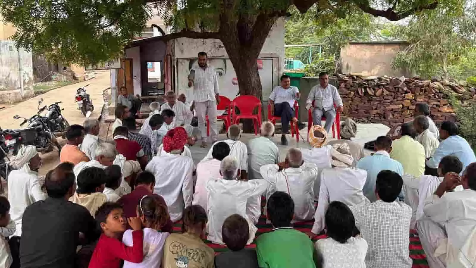 तस्वीर में ग्रामीण लोग पेड़ के नीचे जमीन पर बैठकर किसी बैठक में चर्चा कर रहे हैं। तस्वीर में ग्रामीण लोग पेड़ के नीचे जमीन पर बैठकर किसी बैठक में चर्चा कर रहे हैं।