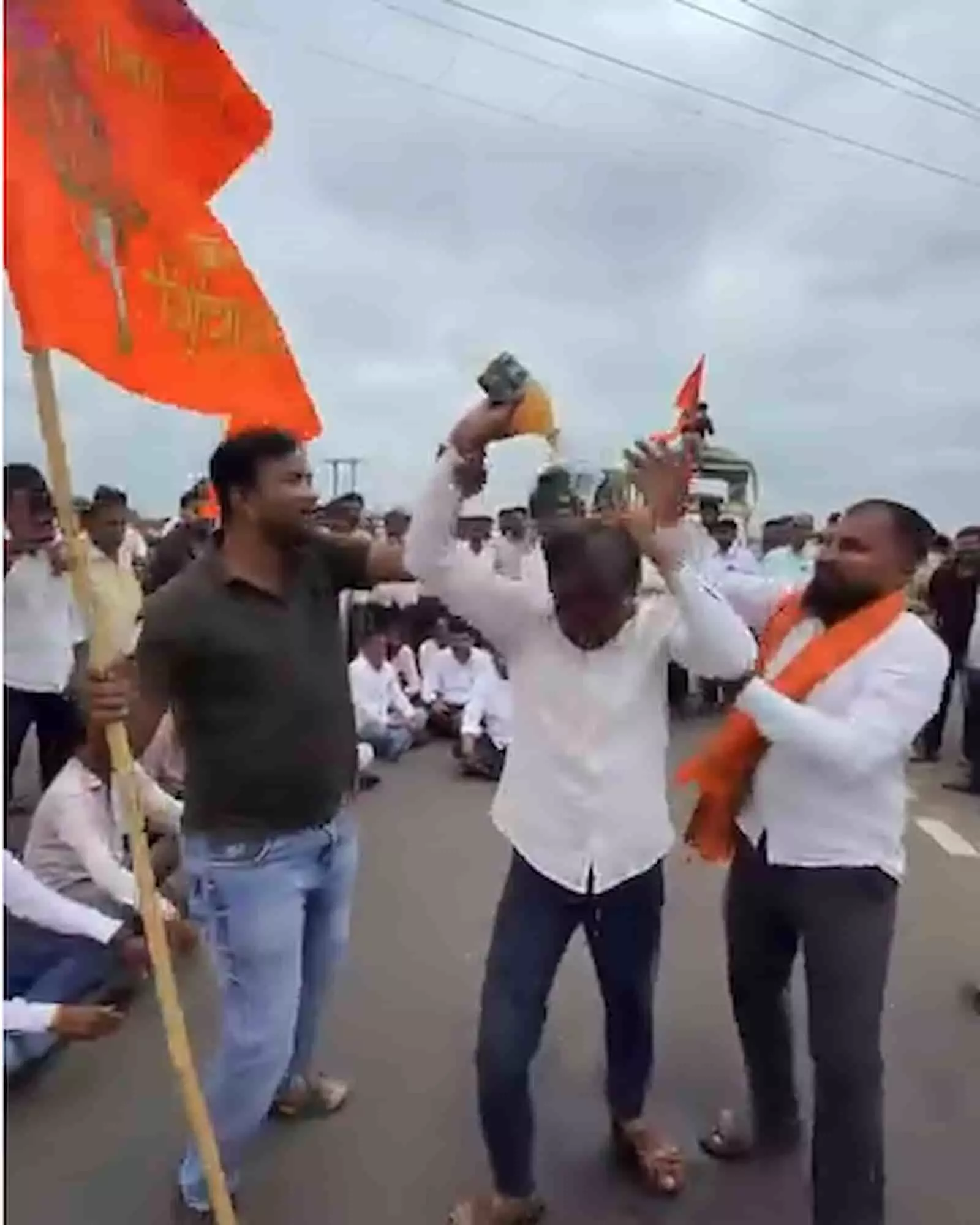 तस्वीर में बाईं ओर झंडा लिए व्यक्ति, बीच में सिर पर केन उड़ेलता युवक और दाएं अन्य लोग खड़े हैं। तस्वीर में बाईं ओर झंडा लिए व्यक्ति, बीच में सिर पर केन उड़ेलता युवक और दाएं अन्य लोग खड़े हैं।