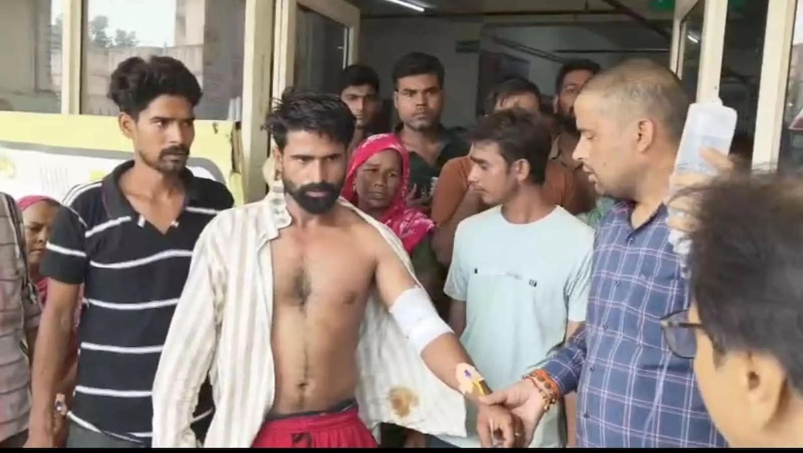तस्वीर में बाईं से दाईं ओर खड़े अन्य लोग और ड्रिप की बोतल पकड़े एक व्यक्ति घायल की मदद कर रहे हैं। तस्वीर में बाईं से दाईं ओर खड़े अन्य लोग और ड्रिप की बोतल पकड़े एक व्यक्ति घायल की मदद कर रहे हैं।