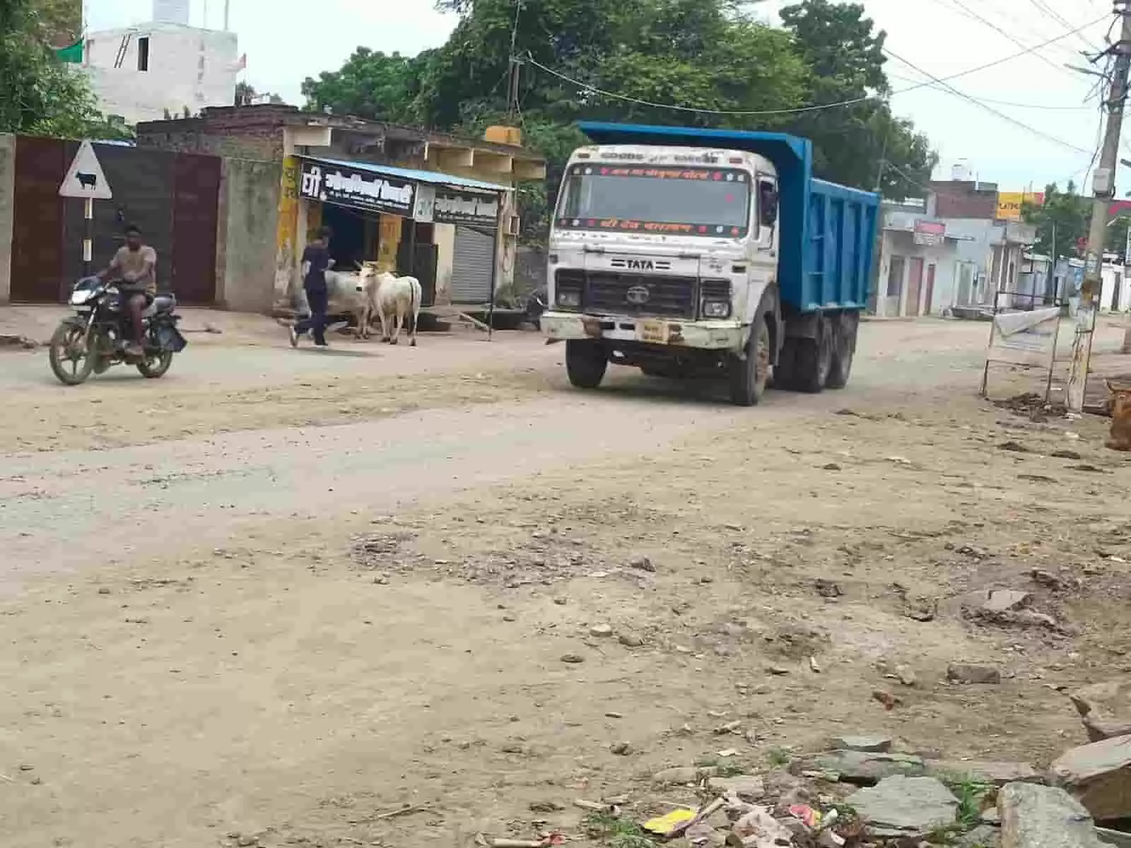 तस्वीर में कच्चे रास्ते से गुजरता डंपर ट्रक और आसपास की दुकानें व राहगीर नजर आ रहे हैं। तस्वीर में कच्चे रास्ते से गुजरता डंपर ट्रक और आसपास की दुकानें व राहगीर नजर आ रहे हैं।