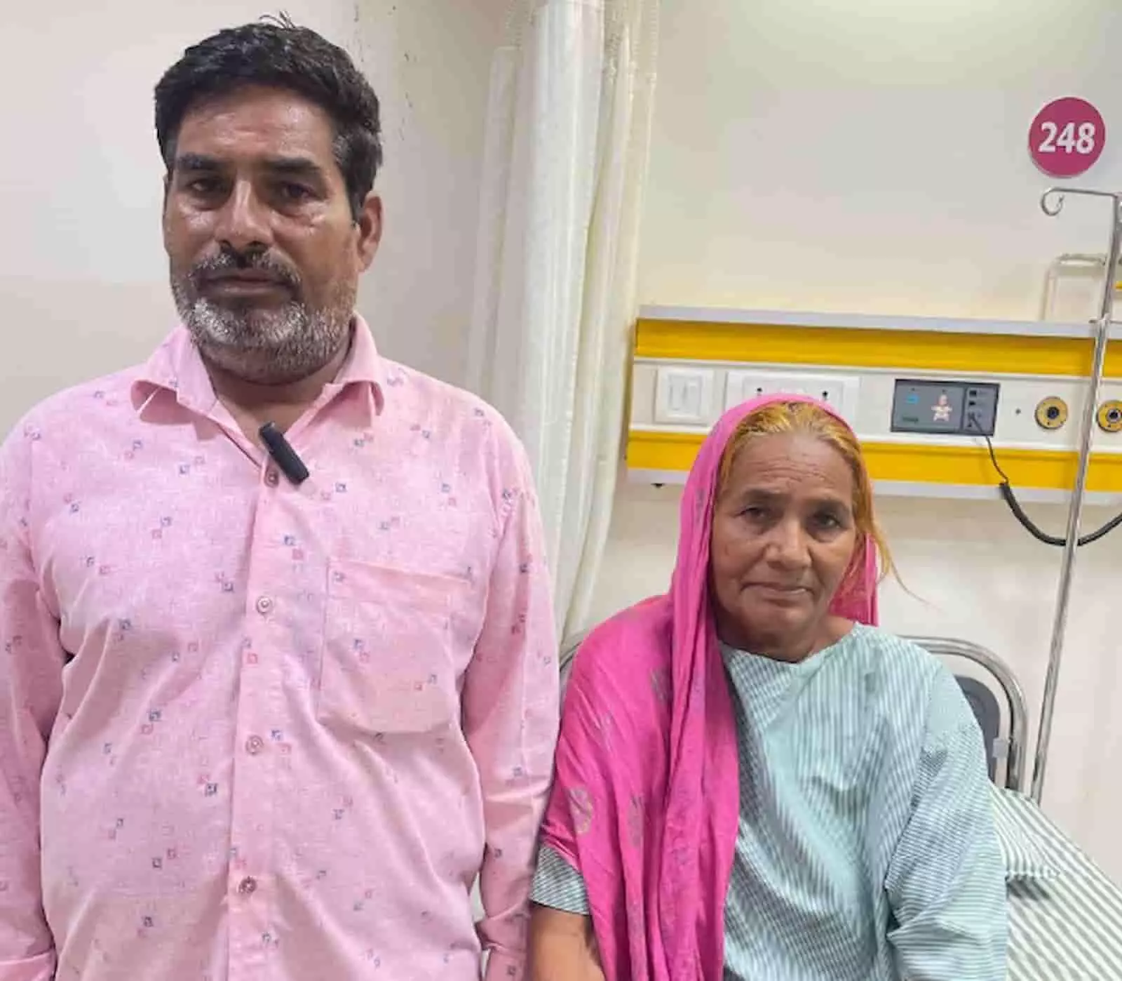 अस्पताल के कमरे में खड़े एक व्यक्ति और महिला मरीज दिखाई दे रहे हैं। अस्पताल के कमरे में खड़े एक व्यक्ति और महिला मरीज दिखाई दे रहे हैं।