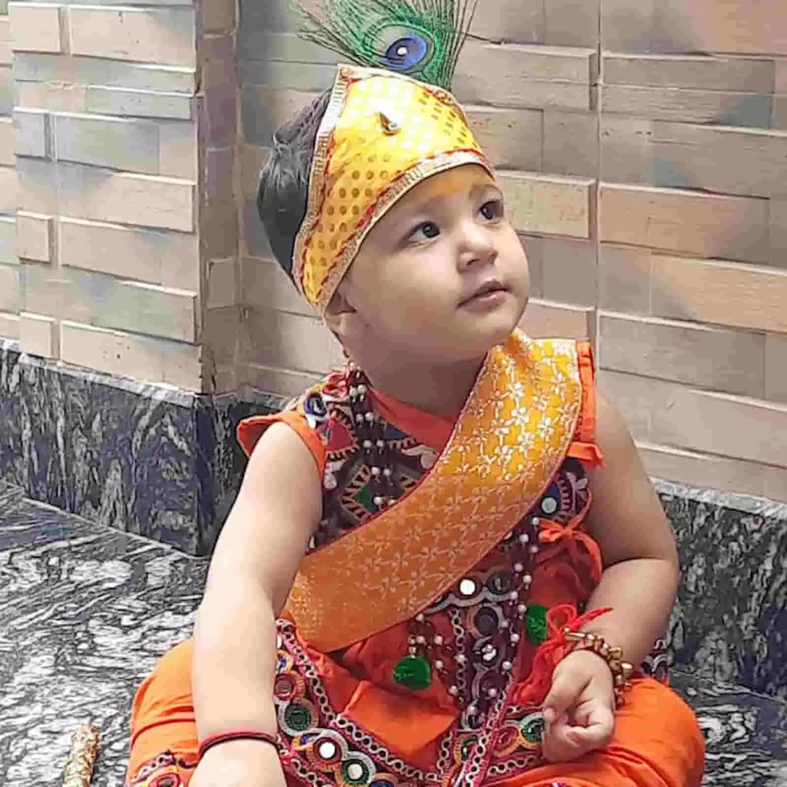तस्वीर में एक बच्चा कृष्ण स्वरूप में पारंपरिक वस्त्र और मुकुट पहने बैठा है। तस्वीर में एक बच्चा कृष्ण स्वरूप में पारंपरिक वस्त्र और मुकुट पहने बैठा है।