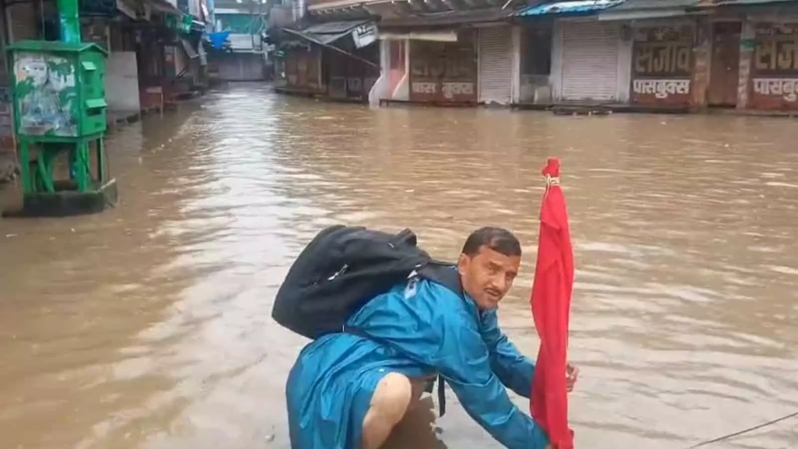 तस्वीर में दिख रही जलभराव वाली सड़क पर एक व्यक्ति सुरक्षा के लिए लाल कपड़ा लगा रहा है। तस्वीर में दिख रही जलभराव वाली सड़क पर एक व्यक्ति सुरक्षा के लिए लाल कपड़ा लगा रहा है।